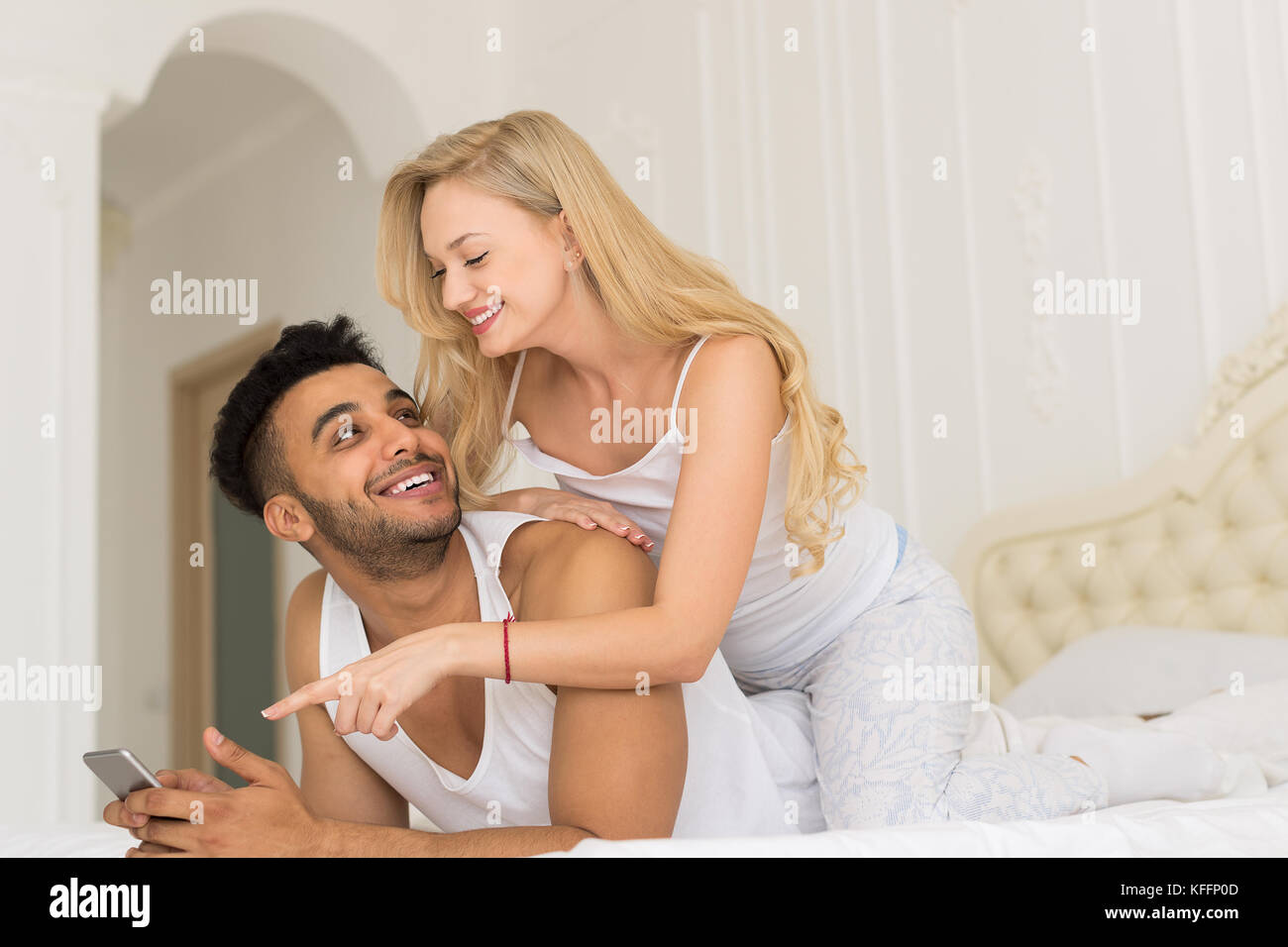 Junges Paar im Bett liegt, glückliches Lächeln Hispanic Mann und mittels smart phone Frau Stockfoto