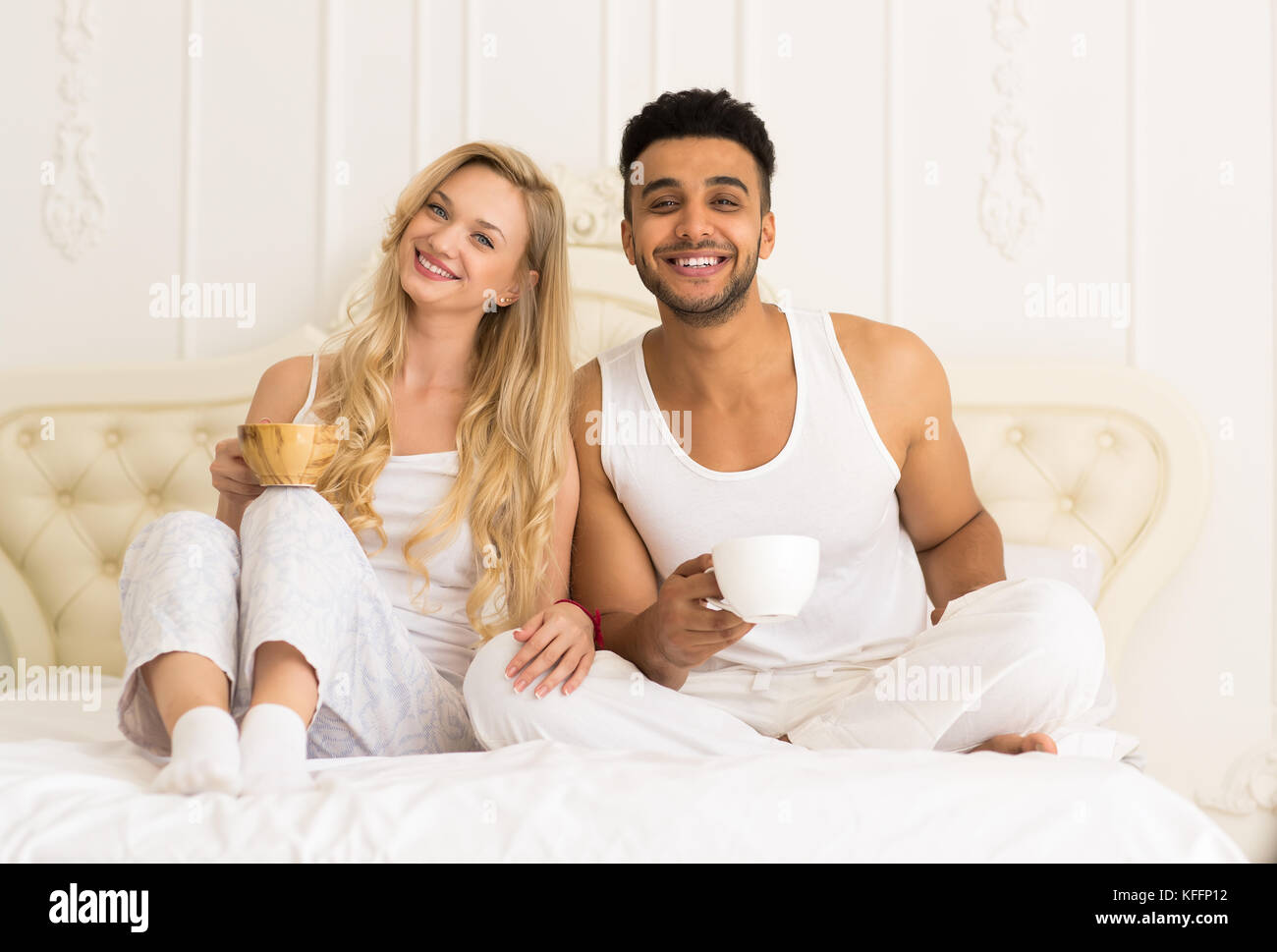 Junges Paar Kaffee trinken Orangensaft im Bett sitzend, glückliches Lächeln junger spanischer Mann und Frau Stockfoto