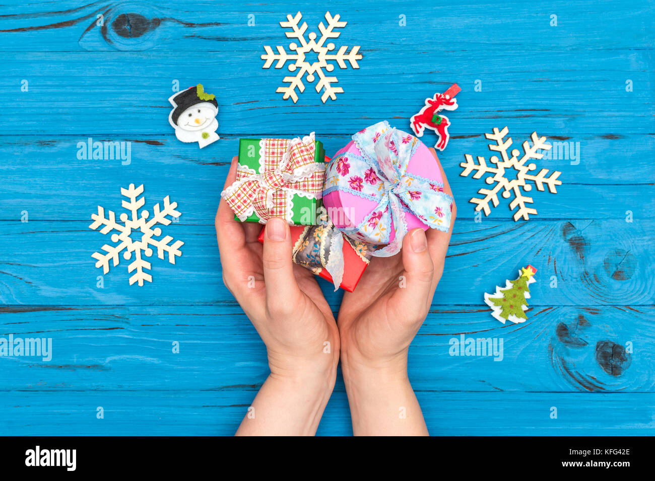 Die Frau Hände mit Geschenk Boxen in der Nähe von Holz- Schneeflocken und Neues Jahr Ornamente auf Blau alte Tabelle Stockfoto