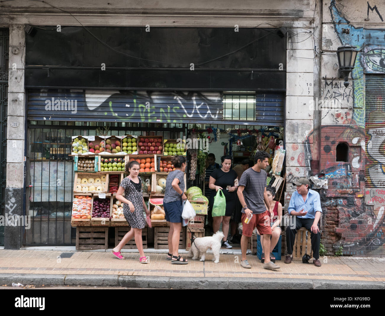 Gruppe von lokalen Käufern vor kleinen Lebensmittelladen sitzt und spricht vor der Front von Obst und Gemüse stehen. Graffiti bedeckt. Stockfoto