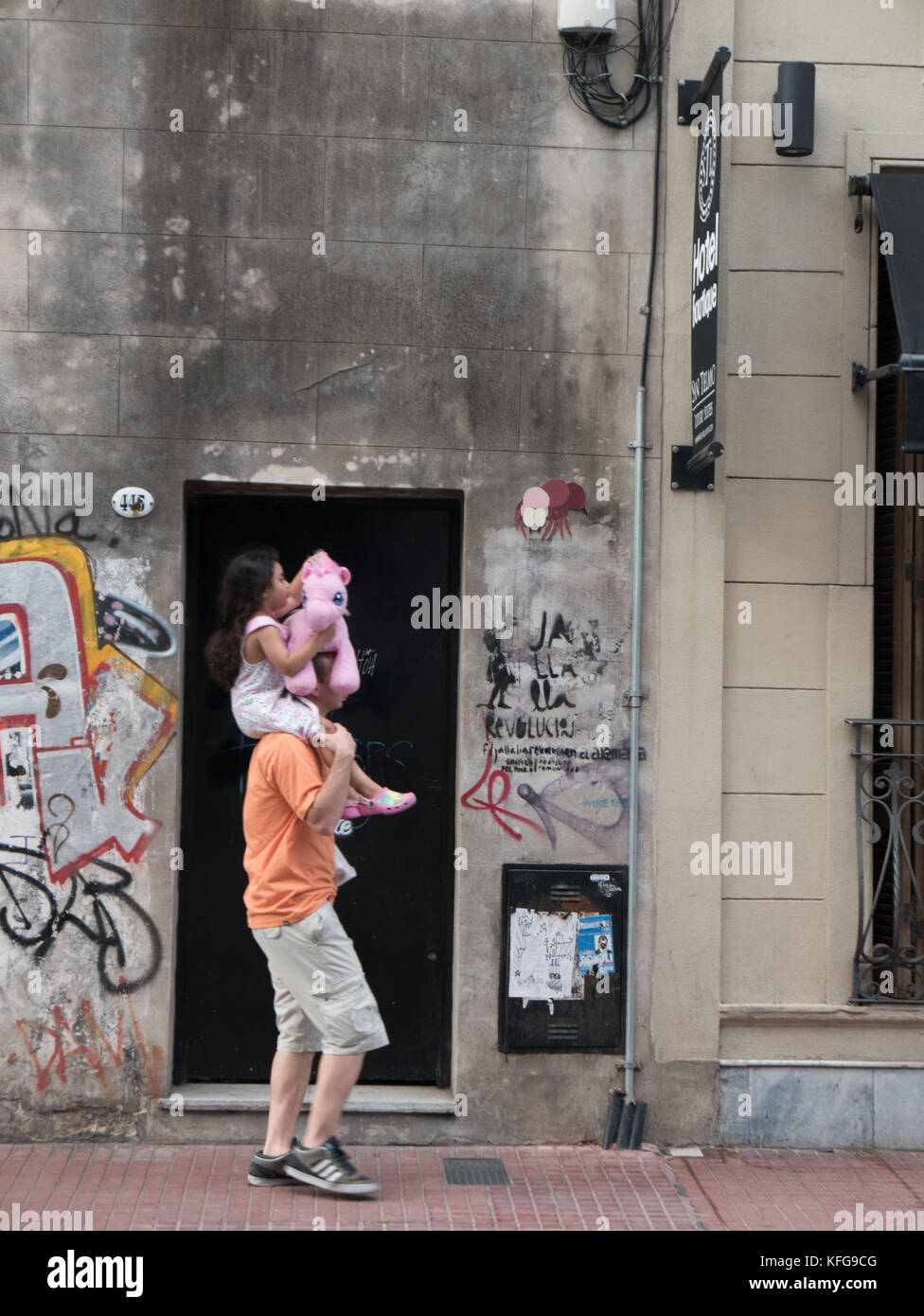 Vater mit Tochter auf die Schultern, als Sie mit einer kleinen Pink Pony Stofftier mit steinernen Gebäude bedeckt mit Graffiti und Street Art. Stockfoto