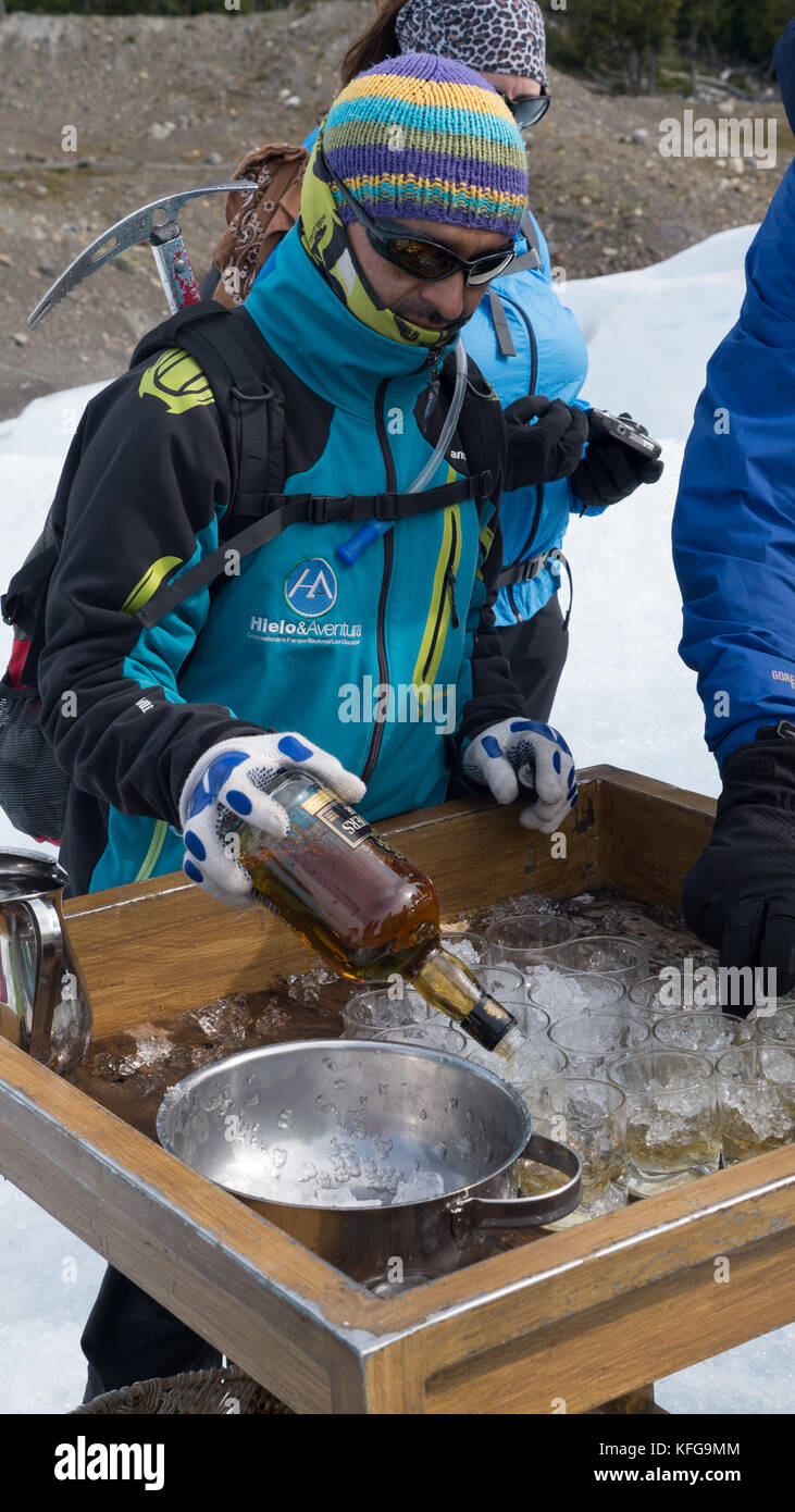 Lokale Reiseleiter poring kleine Gläser Whiskey über Gletscher Eis am Ende der Wanderungen auf Gletscher. Flasche in der Hand mit Eispickel auf den Rücken geschnallt. Stockfoto