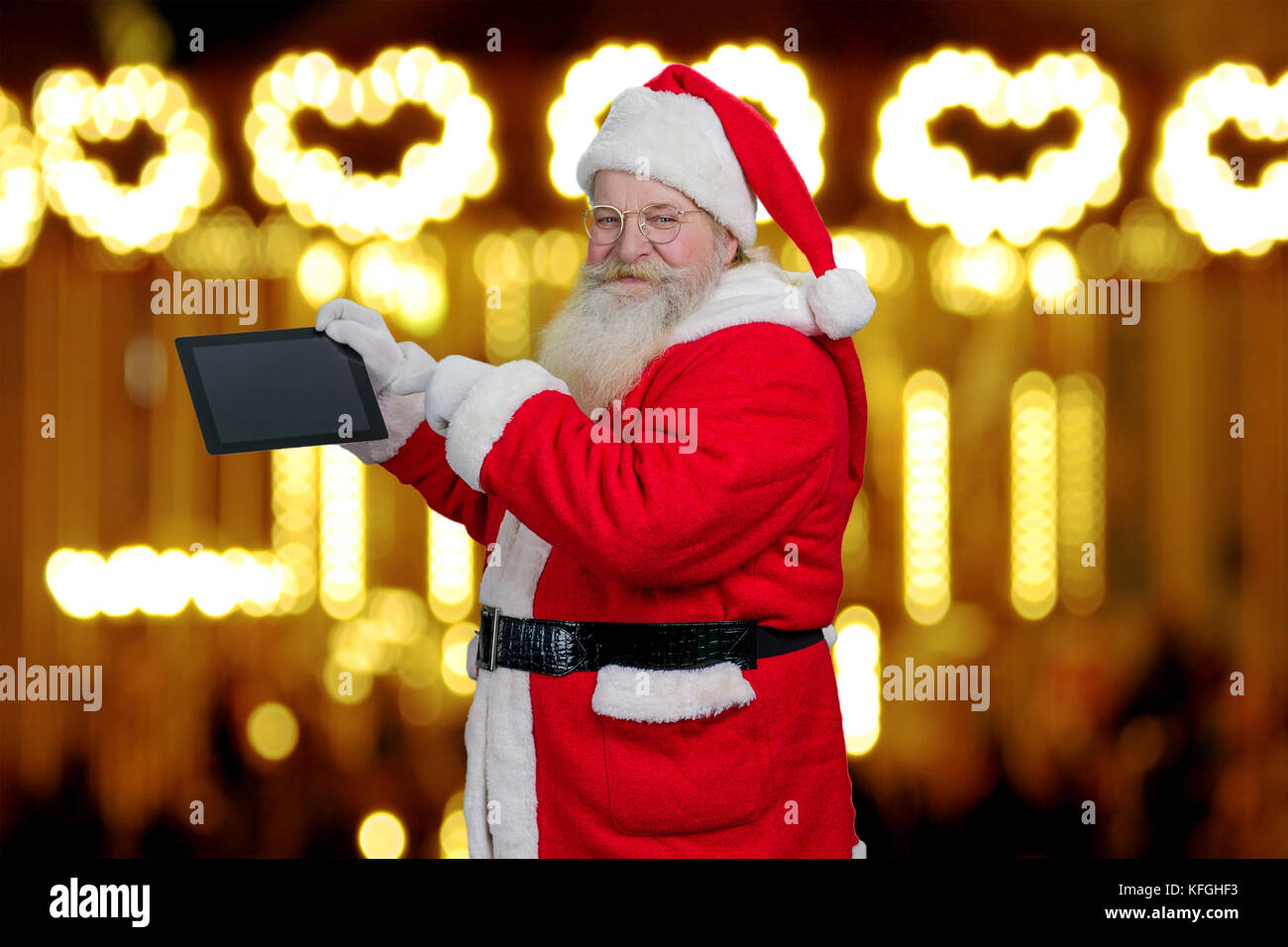 Santa claus Holding computer Tablet. Senior santa claus Holding digital Tablet und das Zeigen mit dem Zeigefinger auf festliche Lichter Hintergrund. Sant Stockfoto