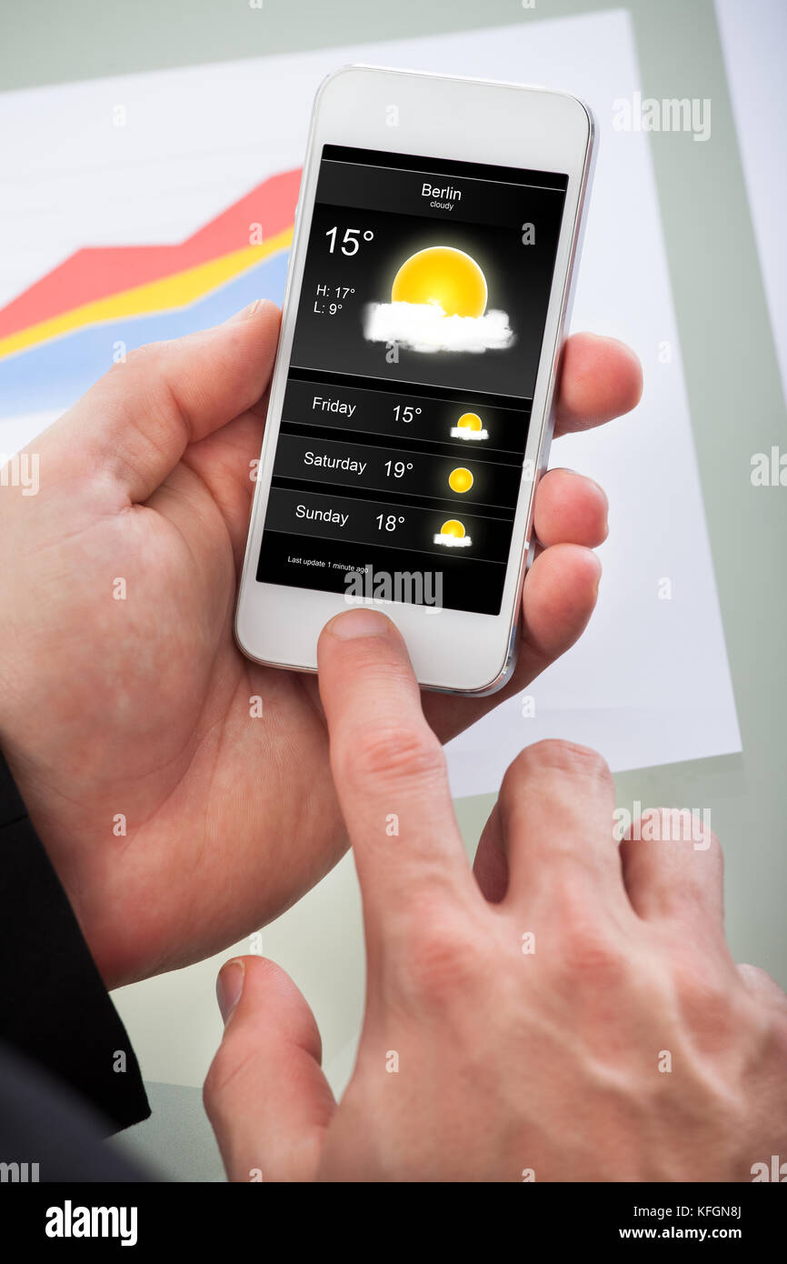 Man Kontrolle der Wettervorhersage für den Tag auf eine Applikation auf seinem Mobiltelefon Ansicht auf dem Bildschirm mit einem bewölkten sonnigen Tag Stockfoto