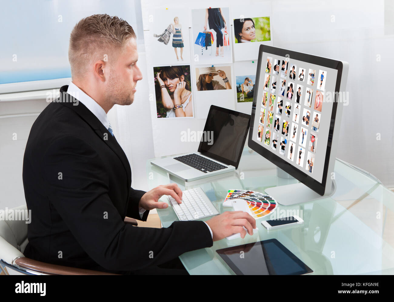Geschäftsmann an seinem Schreibtisch vor einem großen Bildschirm Monitor bearbeiten Fotos sitzen Stockfoto