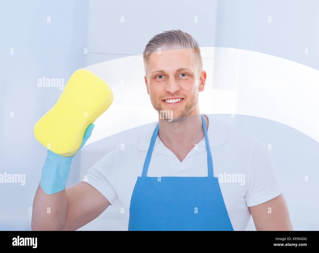 Männliche Hausmeister mit einem Schwamm ein Fenster in einem Büro das Tragen einer Schürze und Handschuhe zu reinigen, da er arbeitet Stockfoto