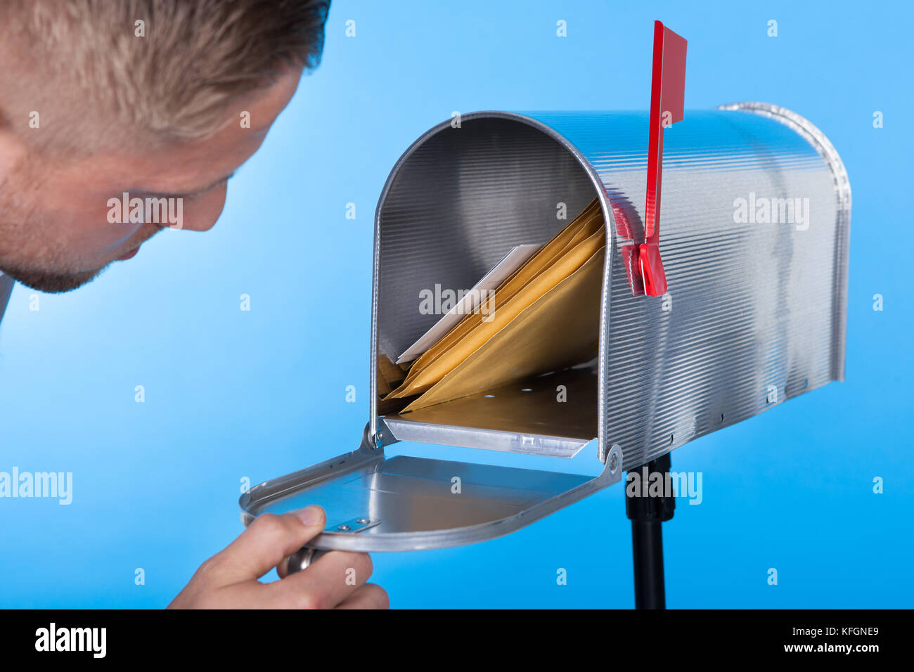 Mann sein Postfach zu öffnen, um e-Mails im Inneren schließen sich seine Hand auf die offene Tür vor einem blauen Himmel entfernt Stockfoto