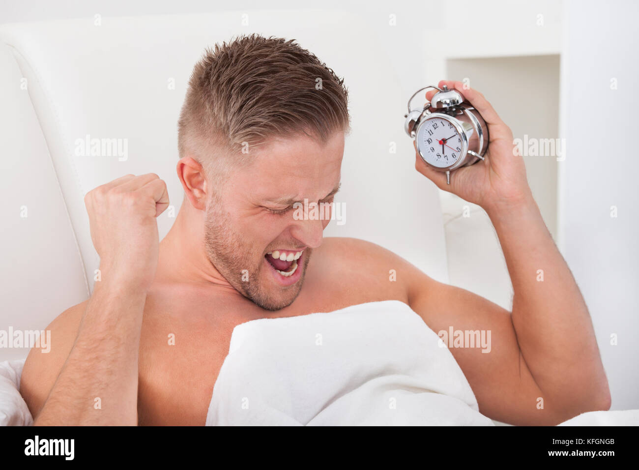 Mann in Frustration über seinen Wecker schreien, wie es ihm nach einer schlaflosen Nacht aufwacht Stockfoto