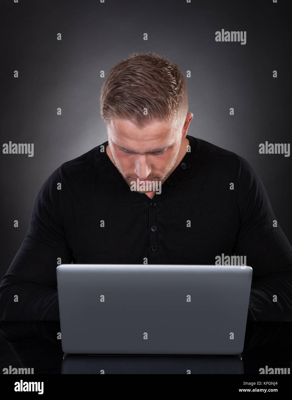 Ein Mann oder Hacker, der nachts an einem Laptop arbeitet und sich im Schein des Bildschirms über die Tastatur beugt, während er im Internet oder im Internet surft Stockfoto