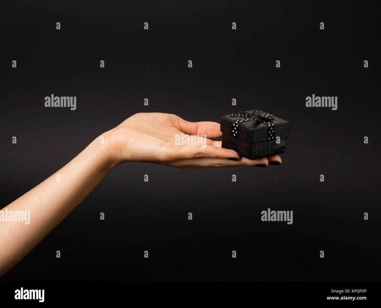 Weibliche Hand, die eine schwarze Geschenkbox mit schwarzen Band verziert mit weißen Tupfen. Auf schwarzem Hintergrund isoliert. Stockfoto