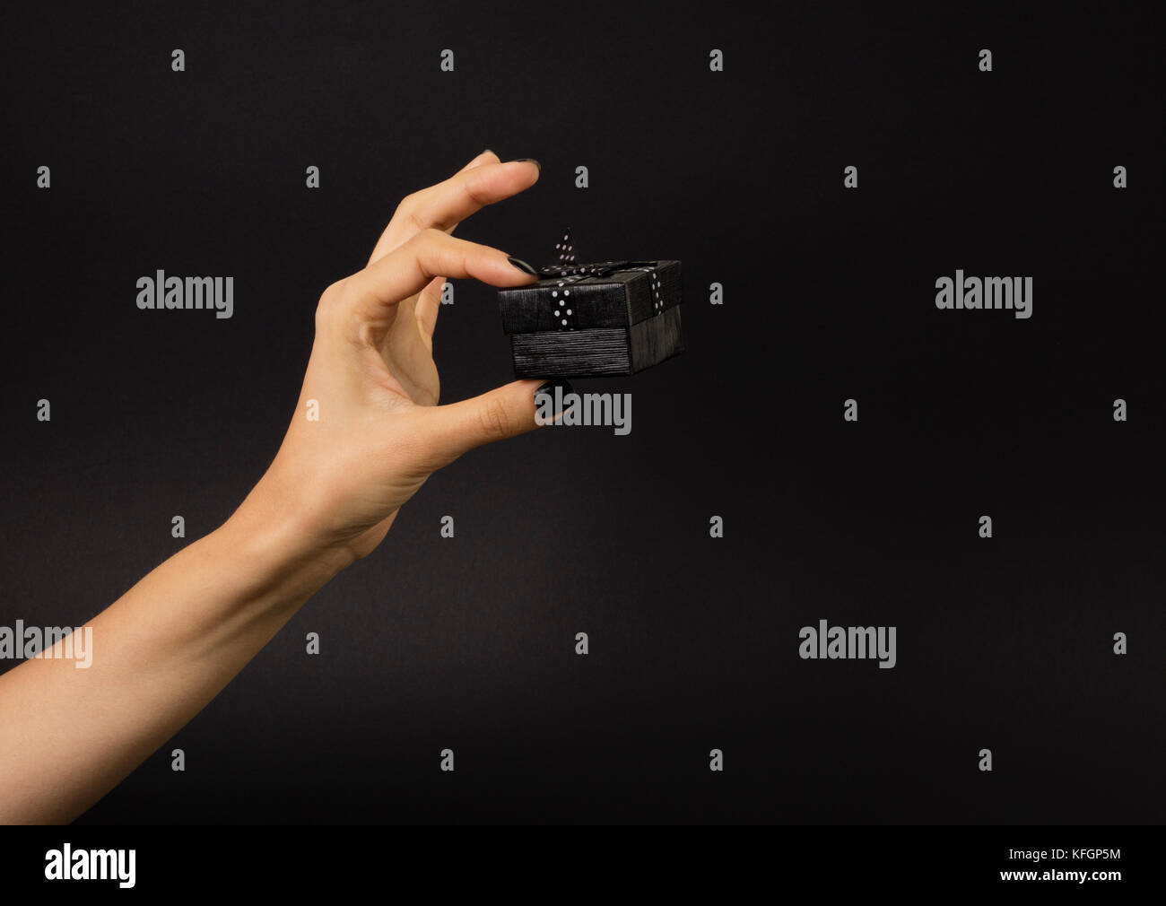 Weibliche Hand, die eine schwarze Geschenkbox mit schwarzen Band verziert mit weißen Tupfen. Auf schwarzem Hintergrund isoliert. Stockfoto
