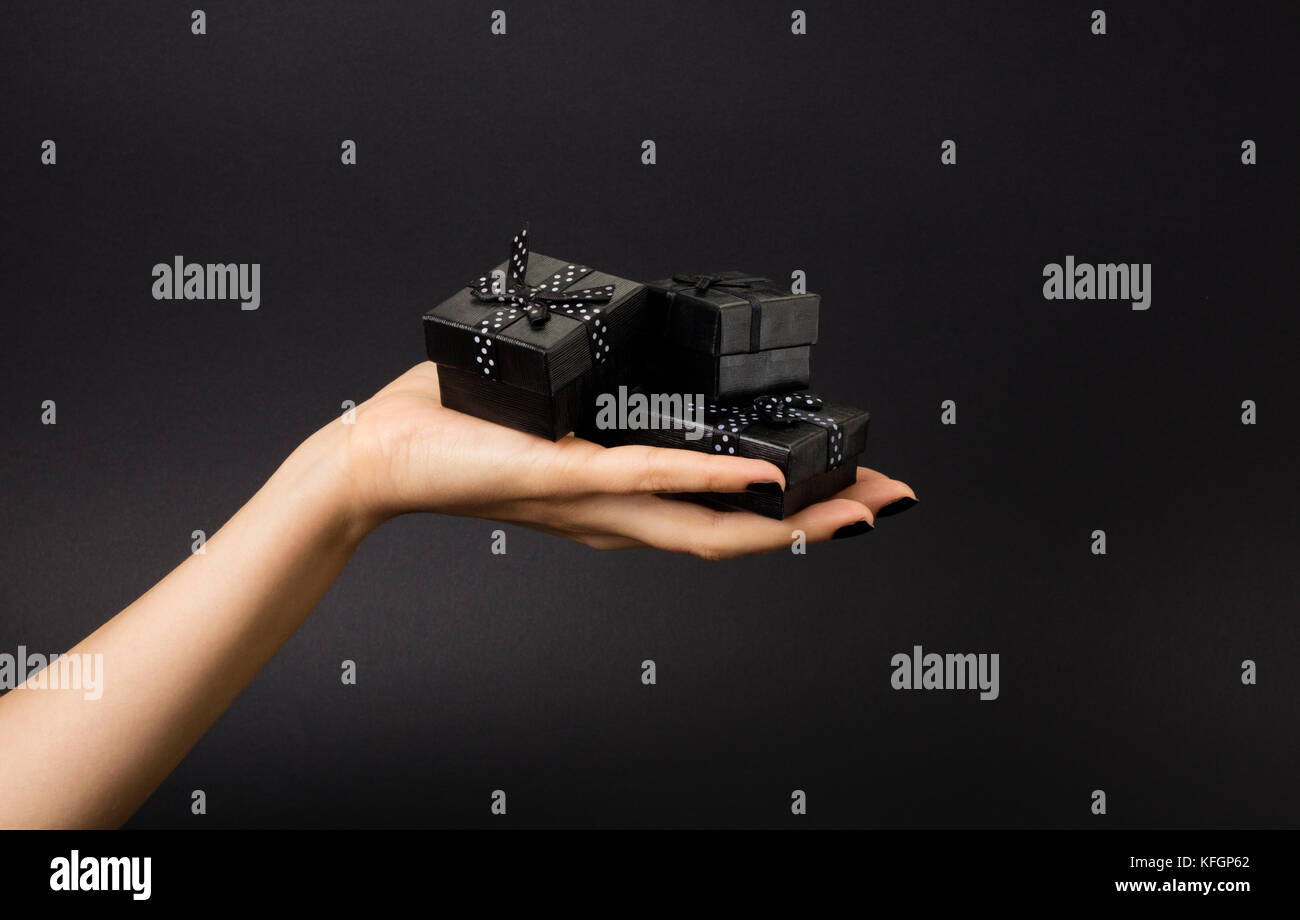 Weibliche hand mit einem drei schwarzen Geschenkboxen auf einem Palm. Auf schwarzem Hintergrund isoliert. geringe Tiefe Foto. Stockfoto