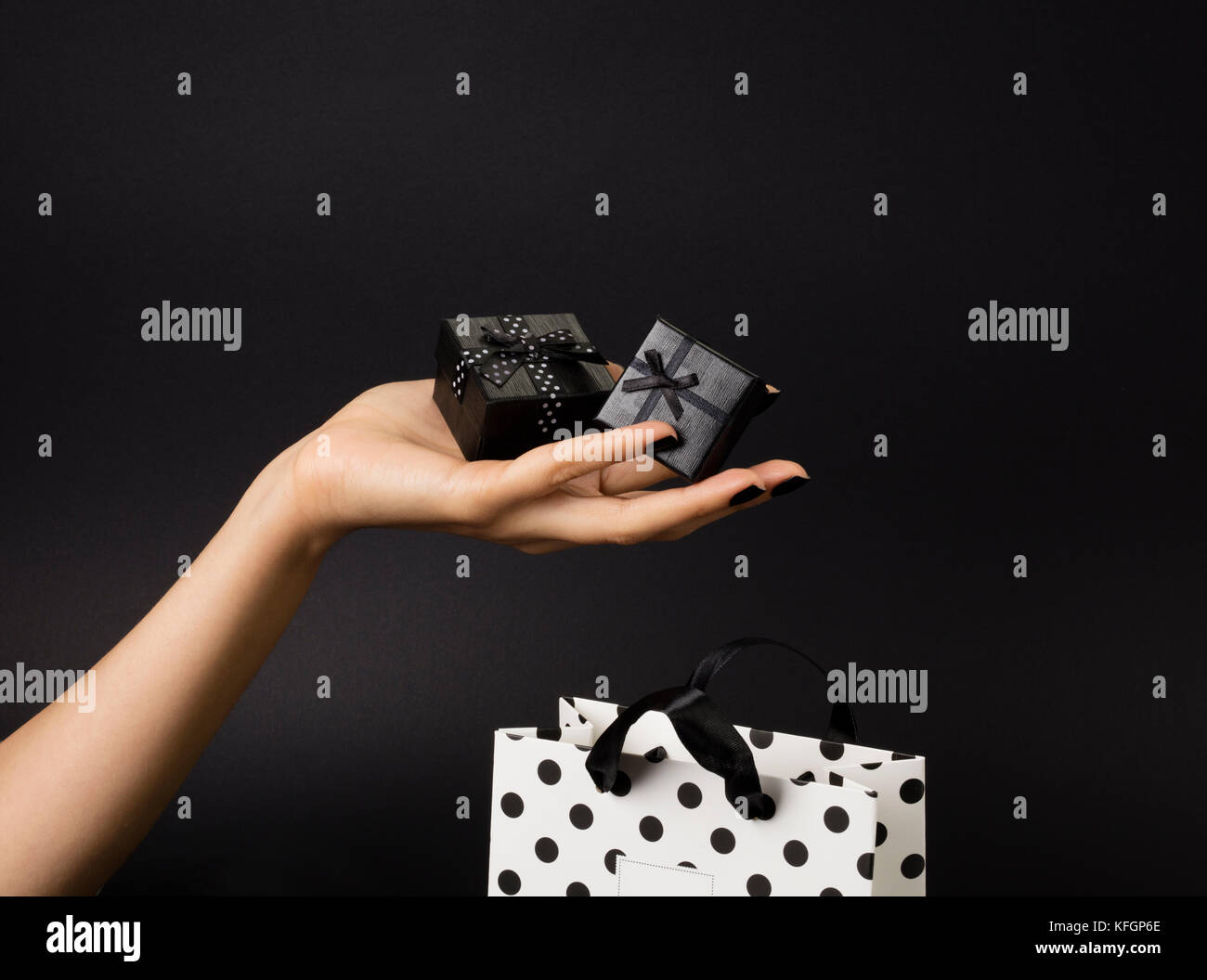 Weibliche hand mit einem drei schwarze Geschenk-Boxen auf einem Palm, schwarz Geschenk-bag dekoriert mit weißen Tupfen unten. schwarzen Hintergrund. Stockfoto