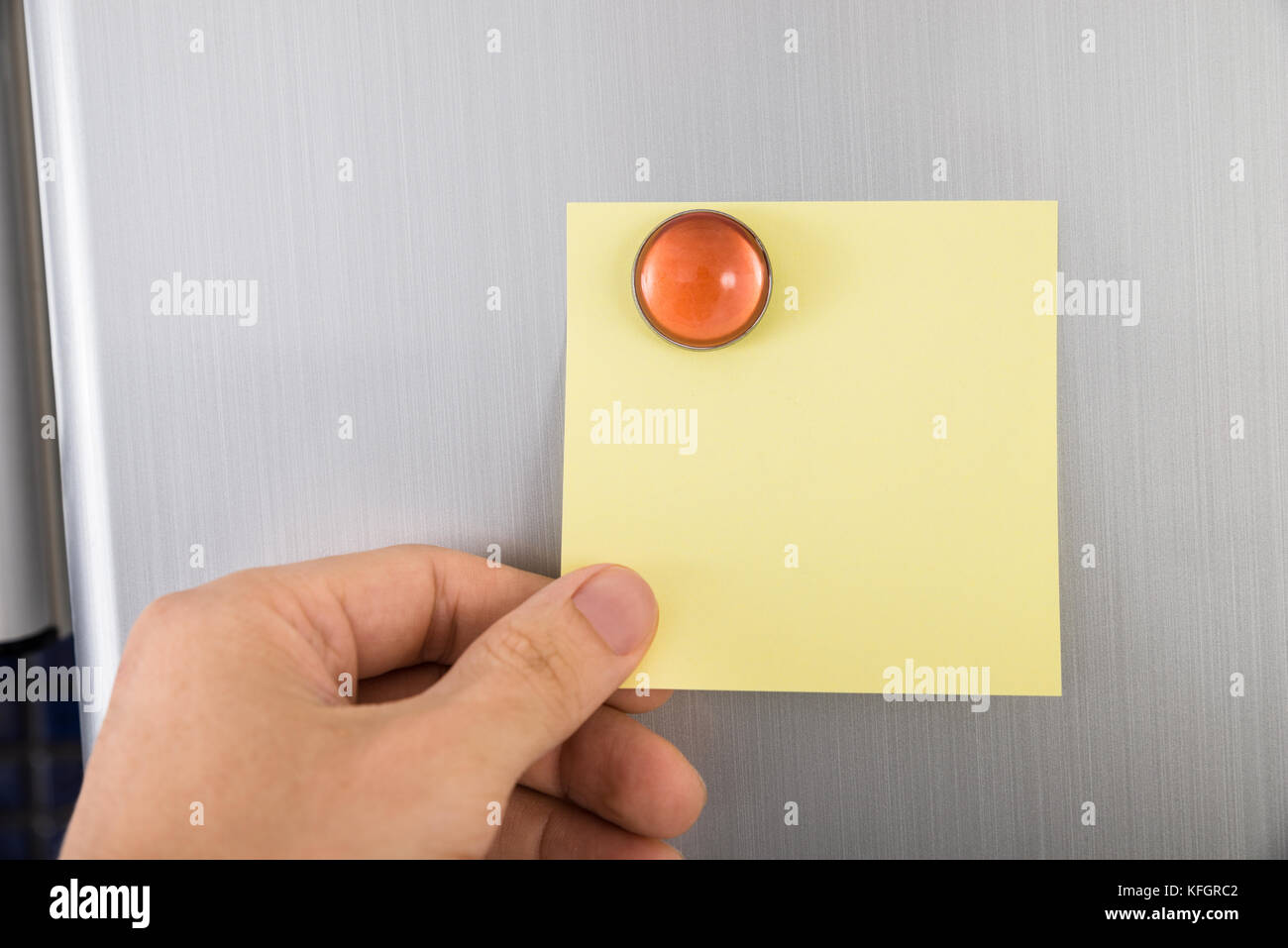 Nahaufnahme der Hand einer Person, die eine leere gelbe Notiz an der Kühlschranktür hält Stockfoto