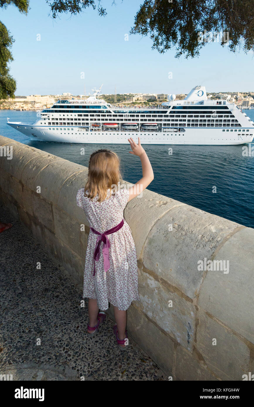 Malta, im Lower Barrakka Gardens, ein siebenjähriges Mädchen Wellen auf Wiedersehen/Abschied von der Kreuzfahrt Schiff, Segeln aus Malta Grand Harbour. (91) Stockfoto