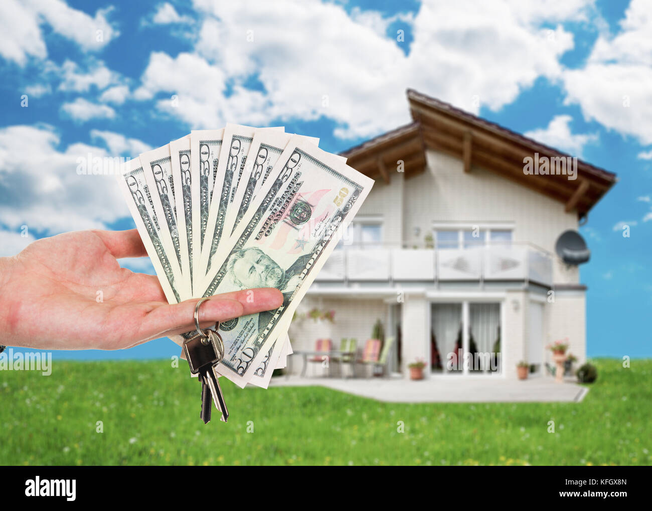 Zugeschnittenes Bild einer Hand, die eine Schlüssel- und Dollar Noten gegen Haus Stockfoto