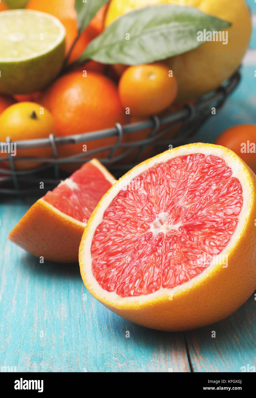 Eine Halbe Grapefruit und andere Zitrusfrüchte: Orange, Zitrone, Mandarine, Limette, kumquat auf einem blauen Hintergrund aus Holz Stockfoto