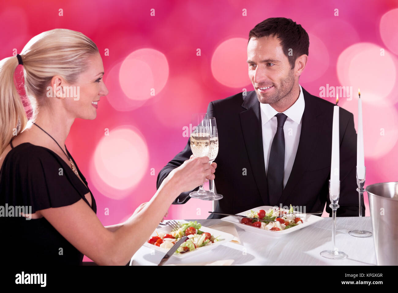 Lächelndes junges Paar, das sich anschaut, während es Champagner-Flöten am Restauranttisch toaste Stockfoto