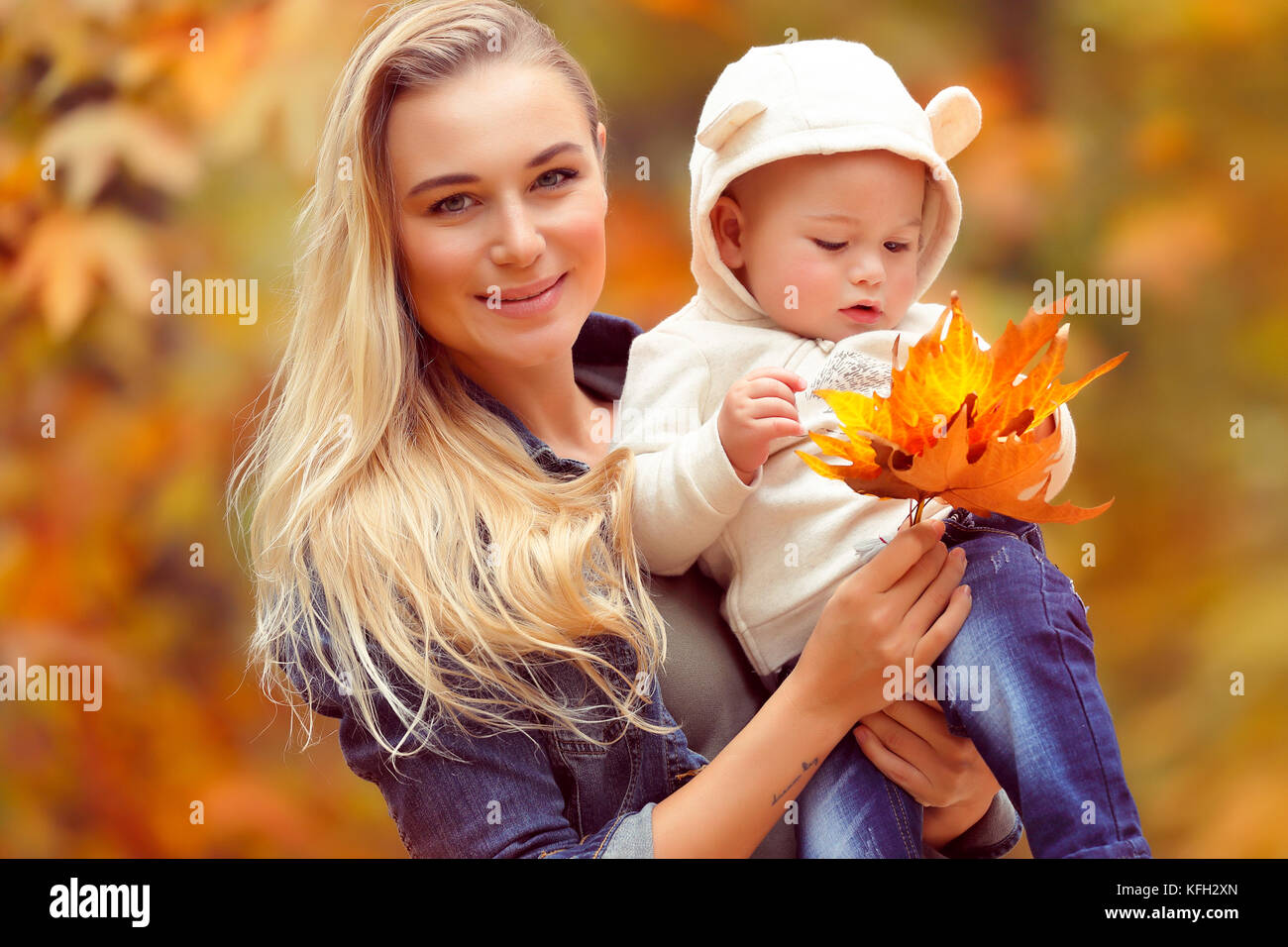 Portrait von eine nette junge Mutter mit Baby in die Hände über herbstliche trockenem Laub Hintergrund, Spaß im Herbst Park und genießen Sie die Schönheit des Herbstes Stockfoto