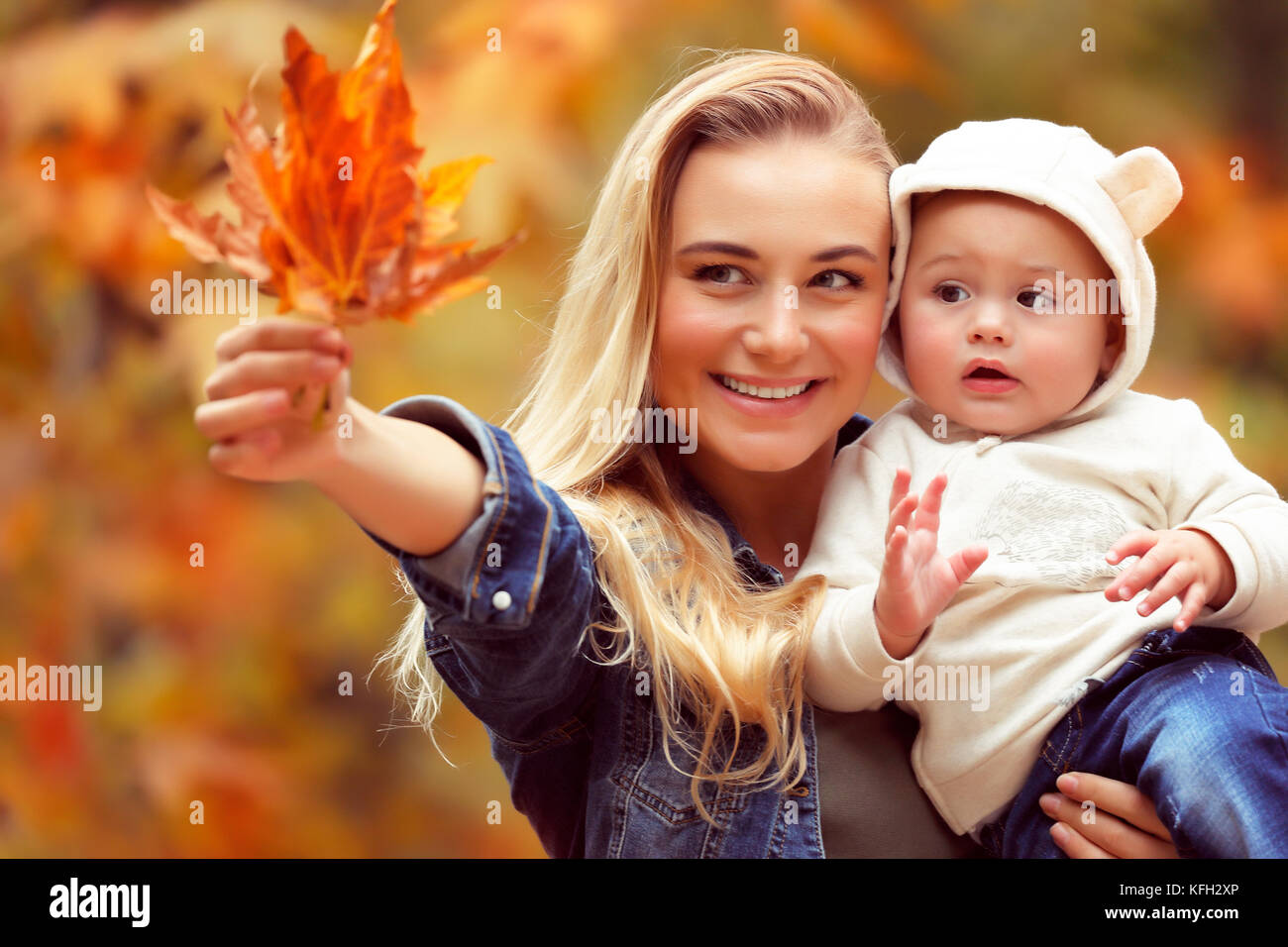 Portrait eines glücklichen Mutter Holding auf Händen ihre kostbaren kleinen Sohn und zeigen ihm trocken Ahornblätter, Spaß im Herbst Park Stockfoto