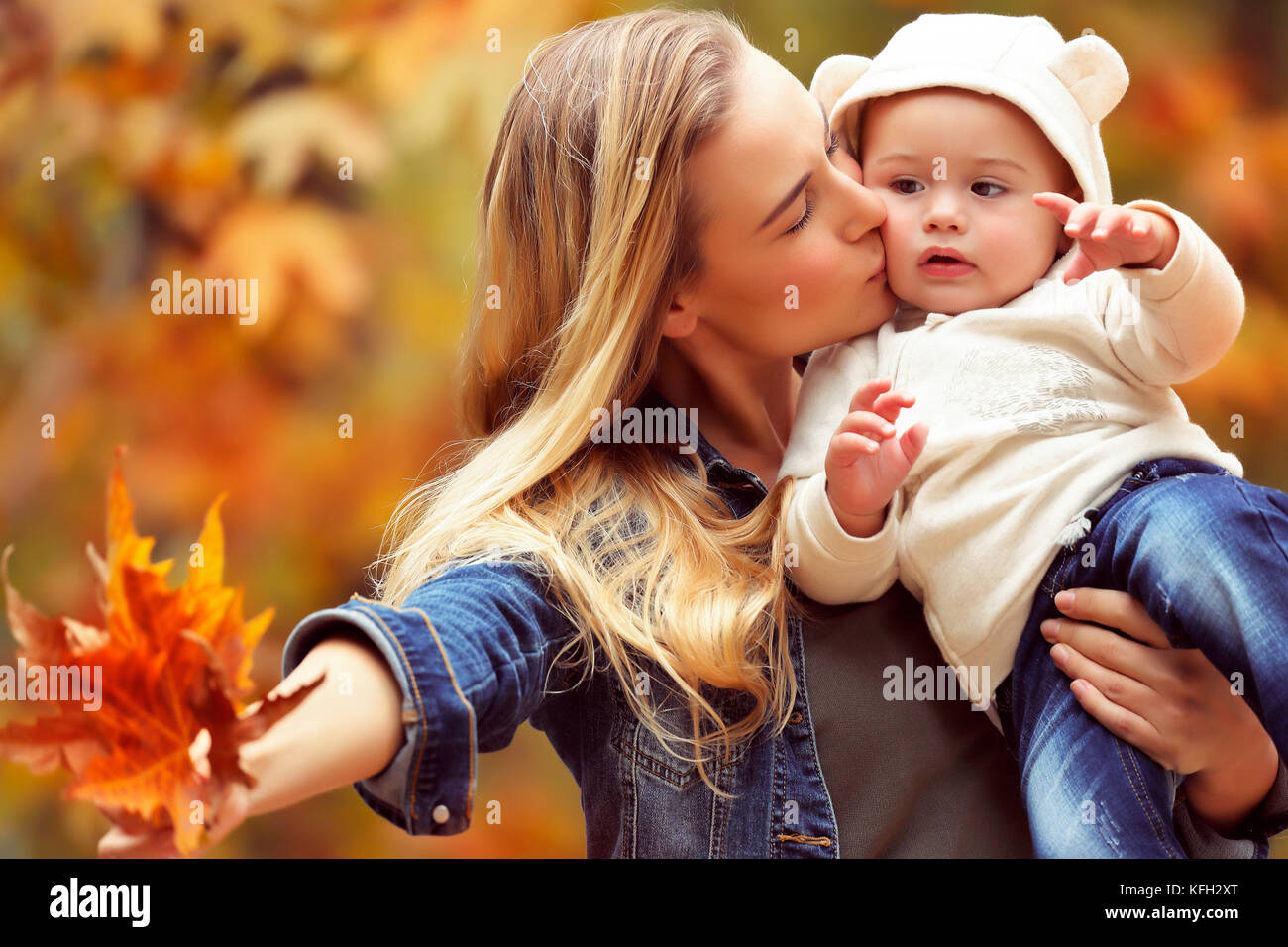 Portrait eines glücklichen Mutter ihre kostbaren kleinen Sohn halten, ihn zu küssen und mit ihm trocken Ahornblätter, Spaß im Herbst Park Stockfoto