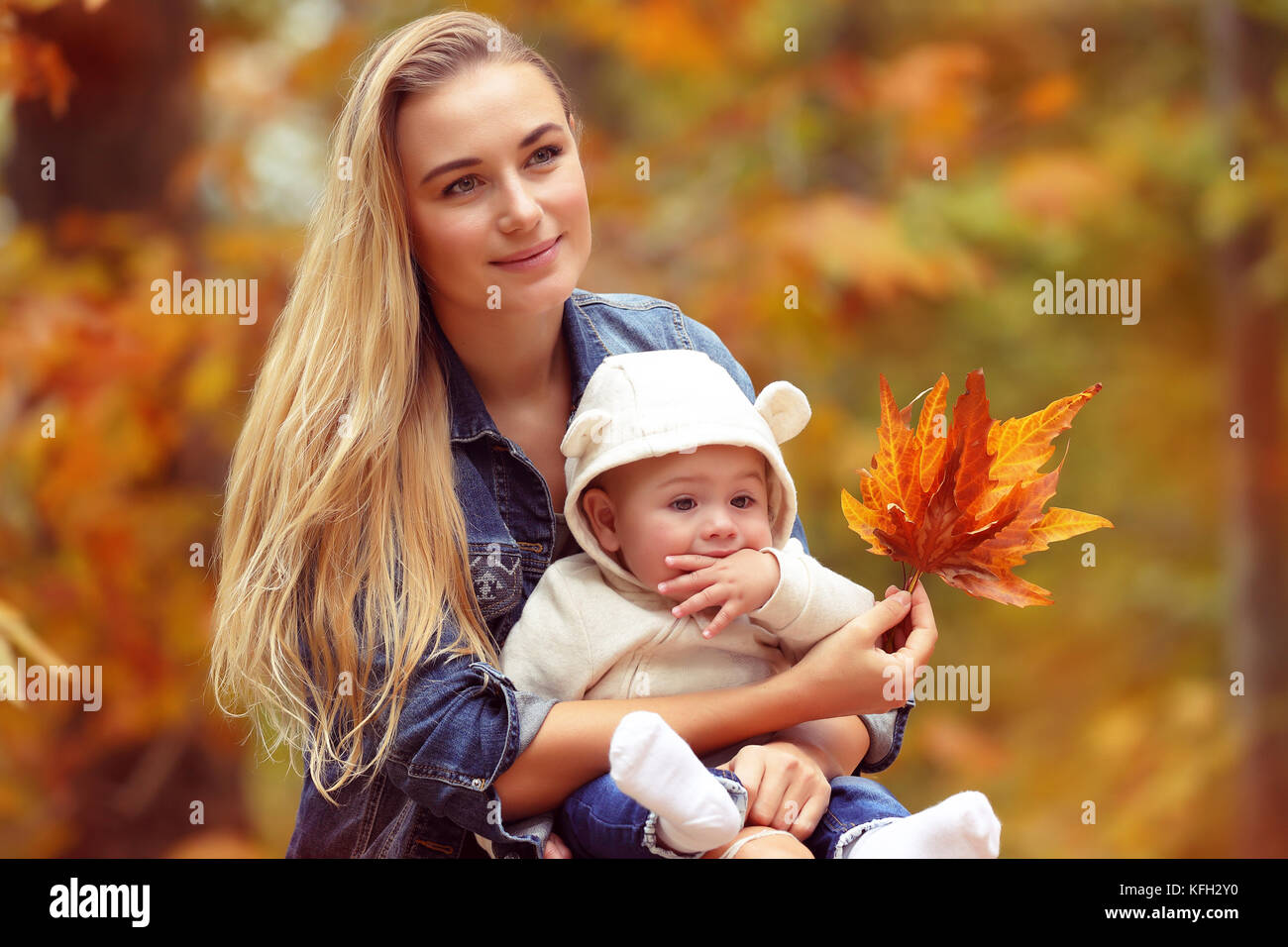 Portrait einer jungen blonden Mutter mit niedlichen kleinen Sohn im Herbst Park sitzen über trockenen baum laub Hintergrund, glückliche Familie mit Freude Ausgaben Stockfoto