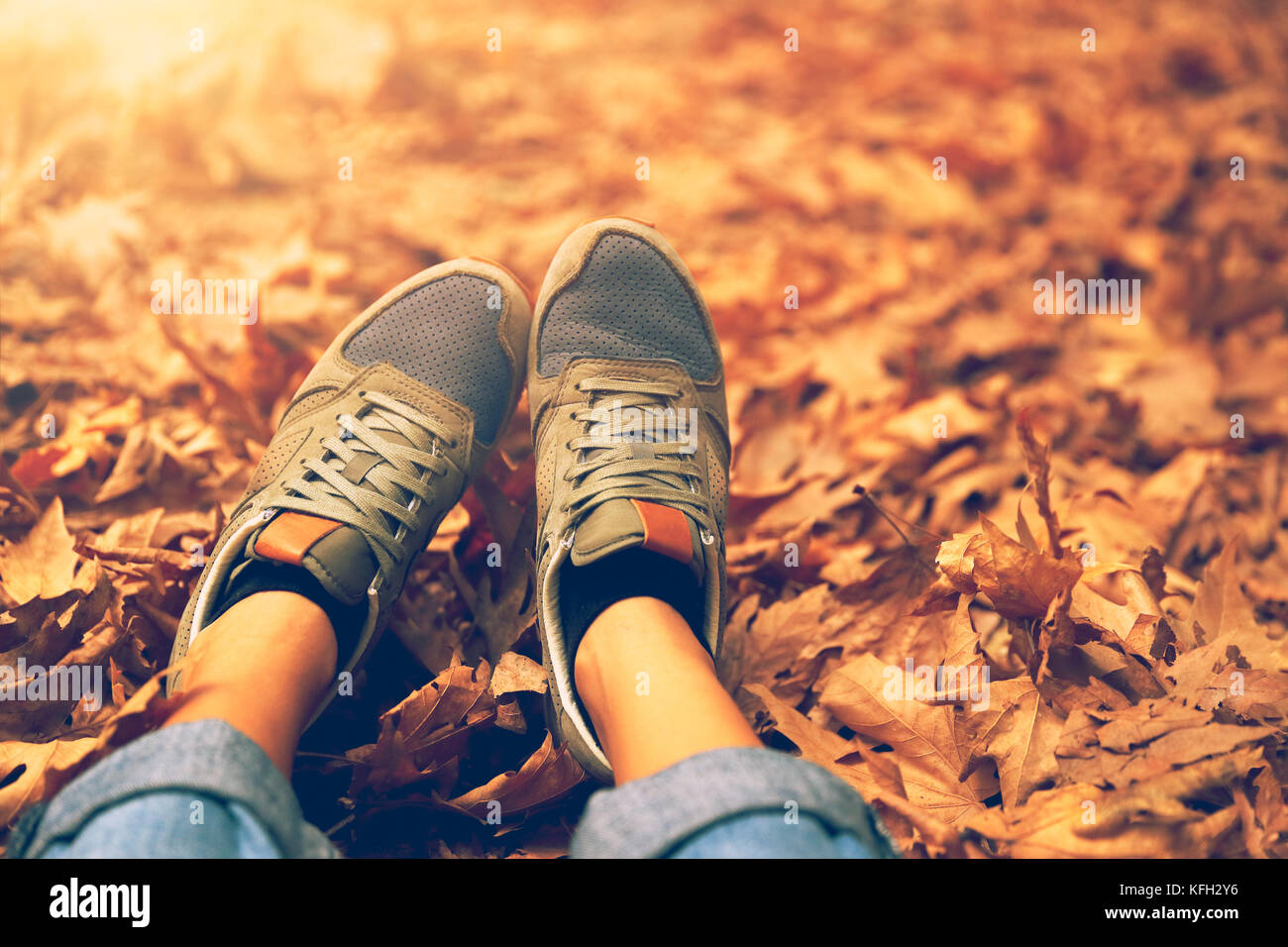 Frauen Füße über trockene Blätter im Herbst Hintergrund, Körperteil, Frau sitzt und entspannt auf dem Boden im herbstlichen Wald in sonniger Tag, genießen Weeke Stockfoto