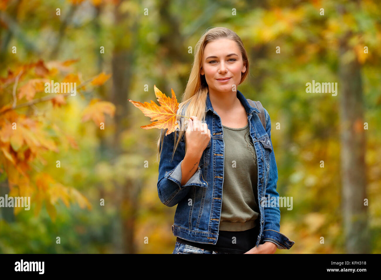 Porträt einer schönen blonden Frau Holding in der Hand schön trocken Gelb maple leaf über herbstliches Laub Hintergrund, Spaß im Herbst Park Stockfoto