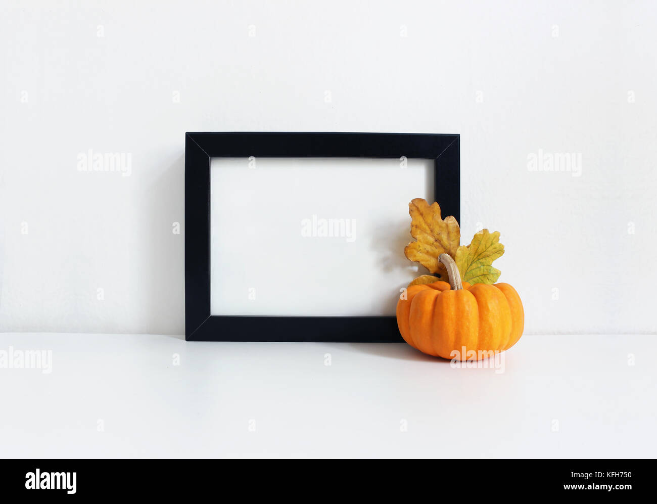 Schwarze leere Holzrahmen mockup mit einem orangefarbenen Kürbis und Golden Oak Blätter liegen auf dem weißen Tisch. Plakat Produktdesign. styled lieferbar feminine Fotografie. Wohnkultur. Herbst, Herbst Konzept. Stockfoto