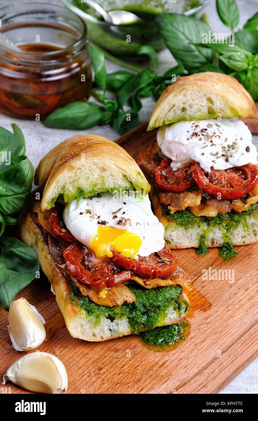 Geröstetes Ciabatta mit Pesto, Scheiben Speck, getrocknete Tomaten und pochiertem Ei Stockfoto