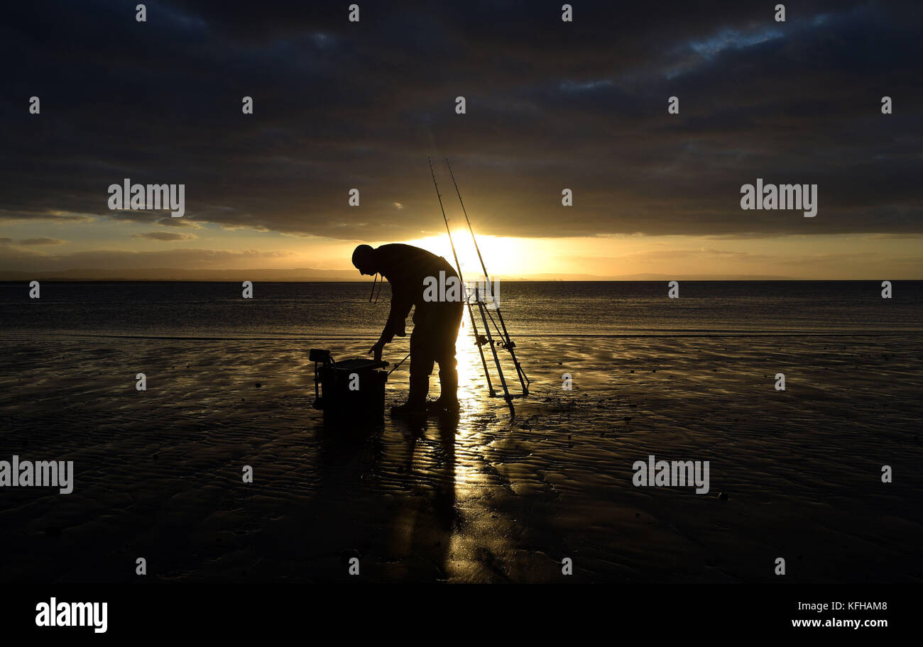 Ein einsamer Angler am Strand von Burnham-on-Sea, Somerset, wie die Sonne eine Stunde früher nach den Uhren wieder eine Stunde in der vergangenen Nacht durch das Ende der Sommerzeit und den Schalter von British Summer Time (BST) der Greenwich Mean Time (GMT). Stockfoto