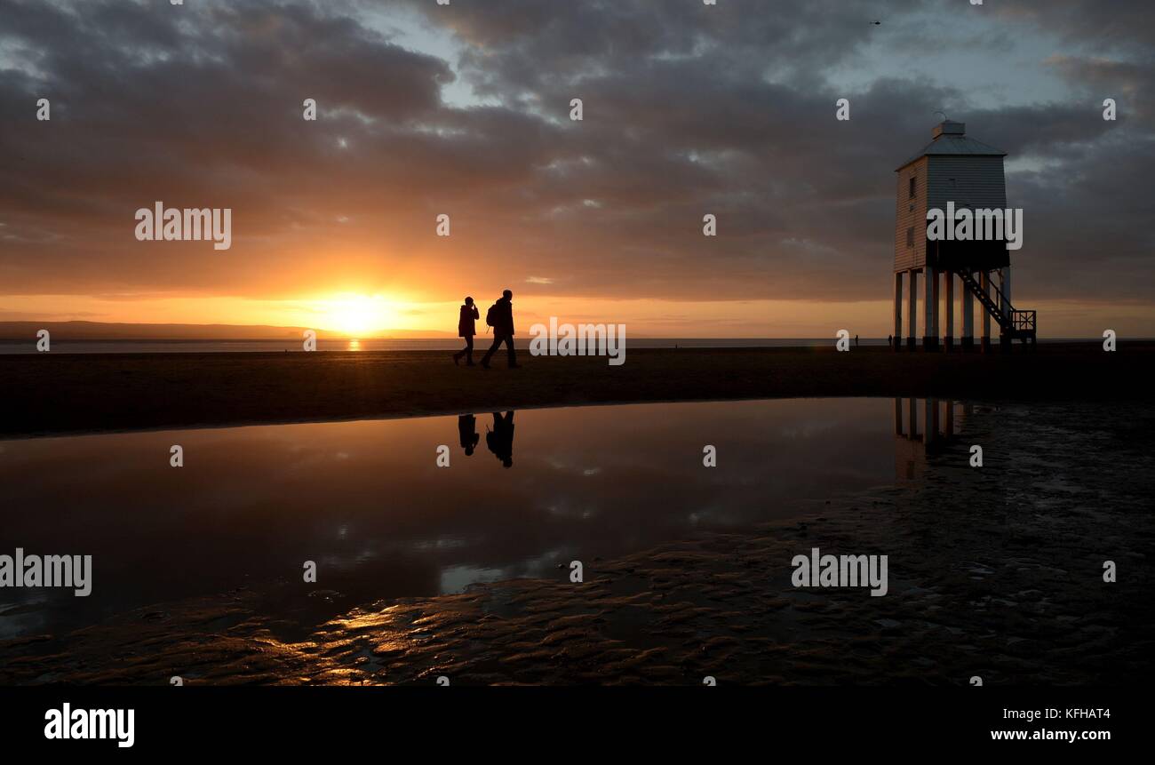 Die Menschen laufen am Leuchtturm in Burnham-on-Sea, Somerset, vorbei, da die Sonne eine Stunde früher untergeht, nachdem die Uhren letzte Nacht eine Stunde zurückgegangen sind, weil die Sommerzeit zu Ende ist und die britische Sommerzeit (BST) auf die Greenwich Mean Time (GMT) umgestellt wurde. Stockfoto