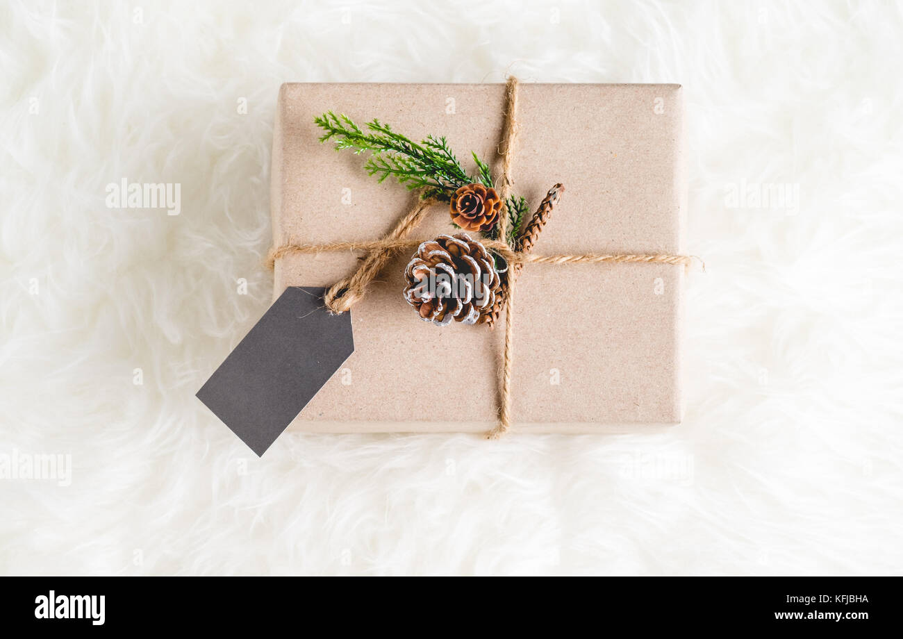 Braunes Papier Handwerk verzogen sich die gegenwärtigen, dekorieren mit Pine Cone und grünes Blatt auf weißem Fell Hintergrund, Geschenk, das für Saisonbedingtes Konzept Stockfoto