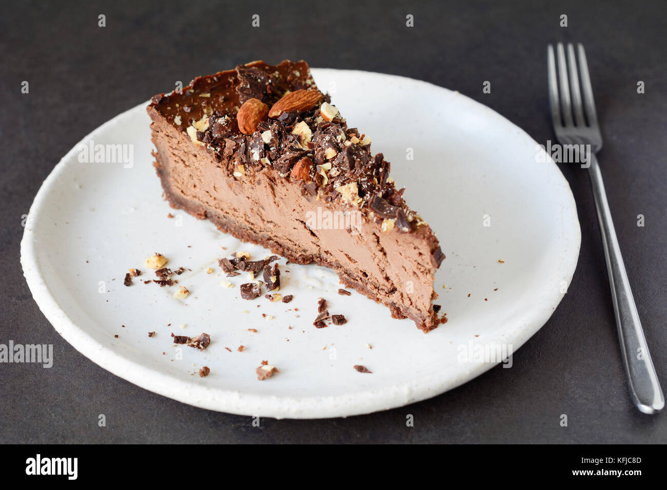 Chocolate cheesecake Slice mit zerquetschten Muttern auf weiße Platte. Stück Schokoladenkuchen Stockfoto