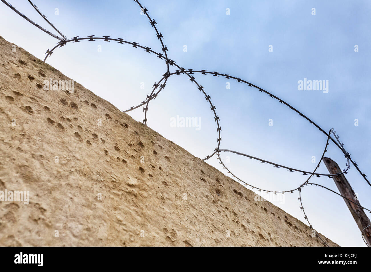 Beton Mauer mit Stacheldraht auf dem Hintergrund einer ruhigen blauen Himmel. Stockfoto