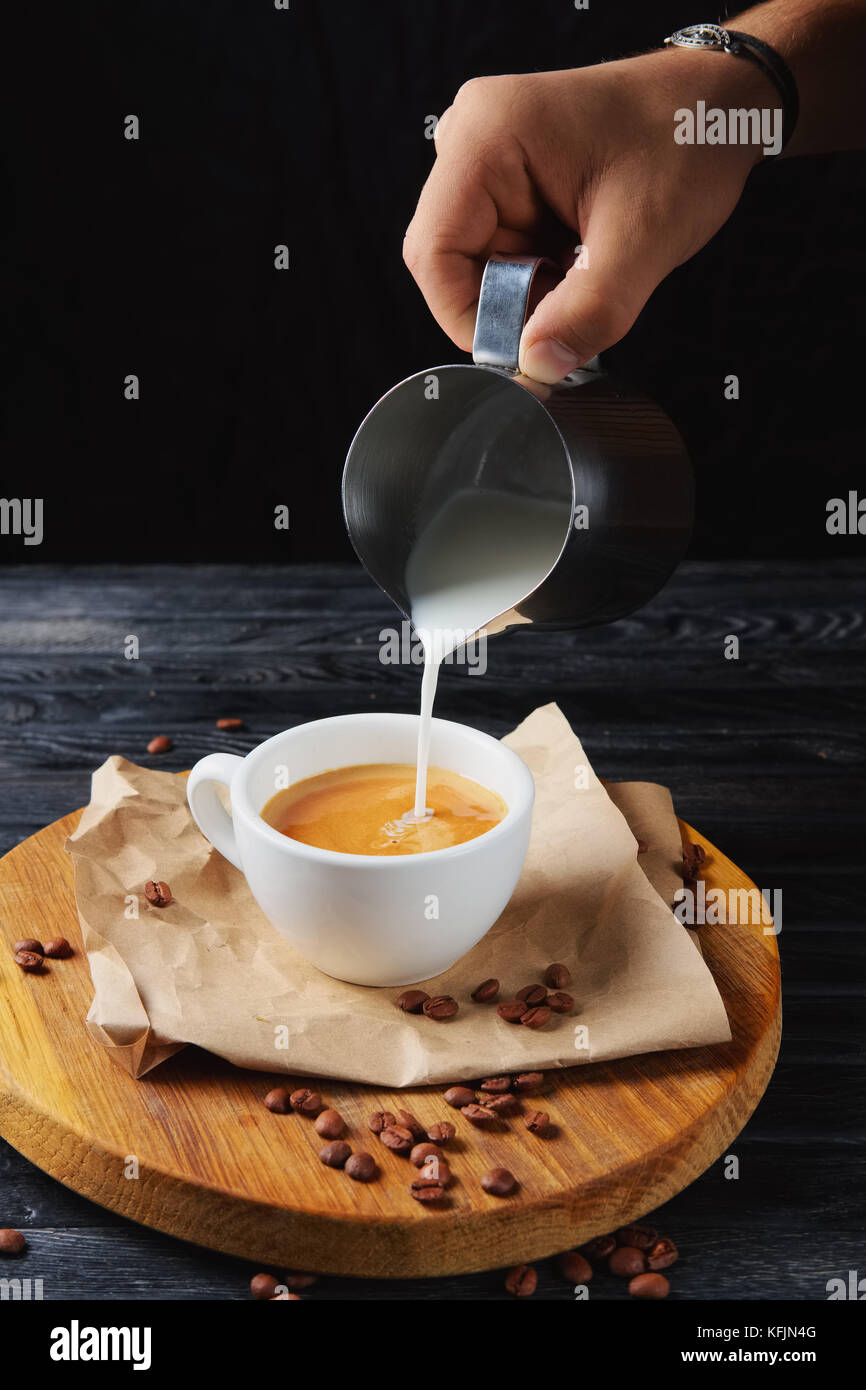 Gießen Milch in Kaffee Tasse mit Cappuccino auf Holzplatte Stockfoto