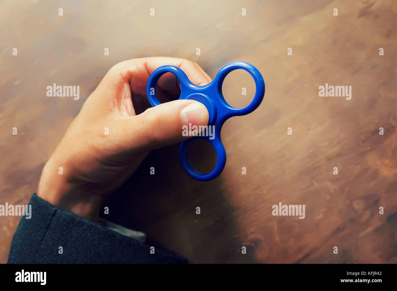 Ein Mann hand Halten einer Hand Spinner oder zappeln Spinner auf dem Hintergrund der hölzernen Tisch. Leistungsstarke Spinner, Twister für Hände Unterhaltung rotierende Spielzeug. Stockfoto