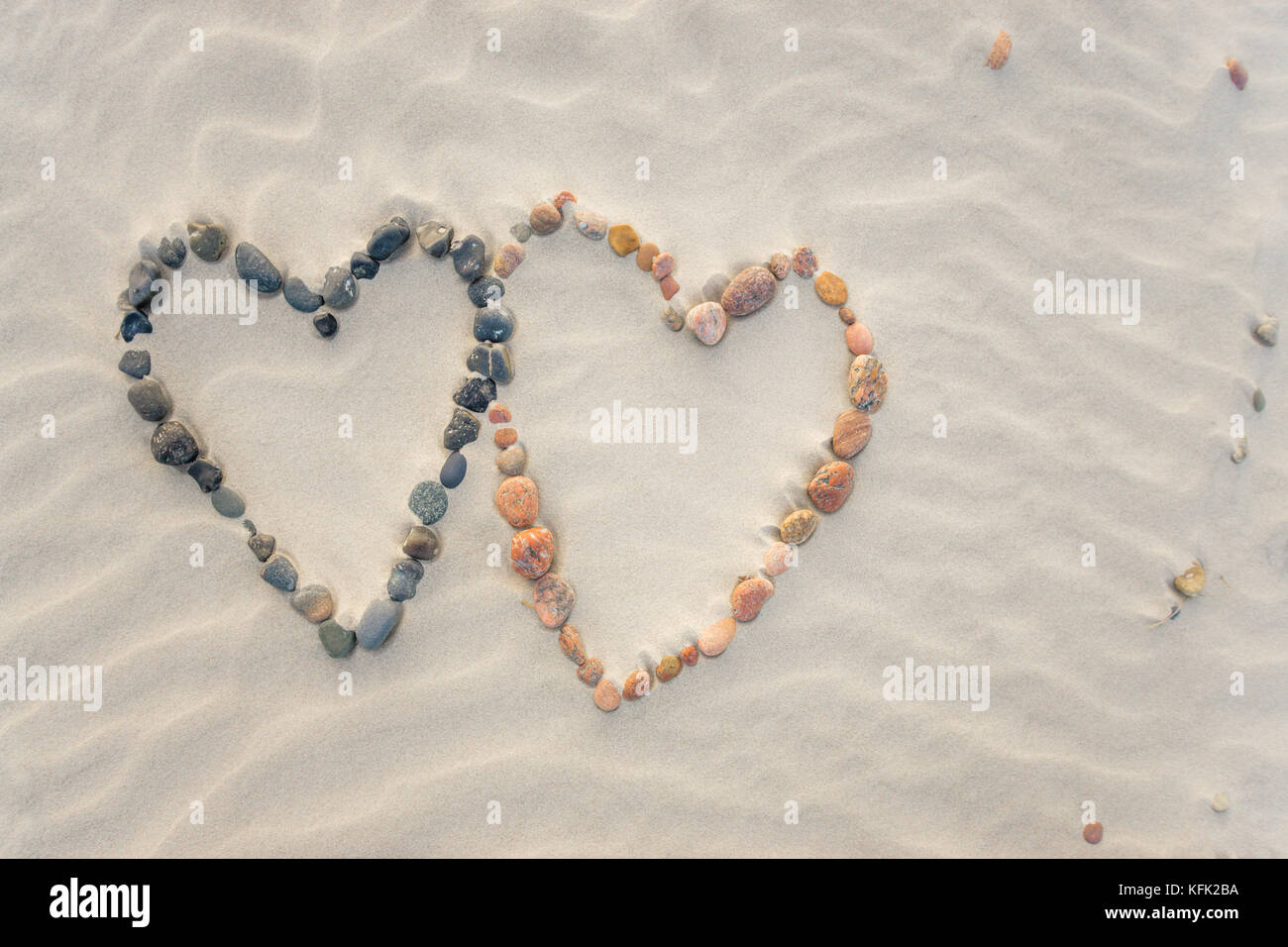 Pebbles angeordnet in Form von zwei Herzen auf Sand strand Wellen Stockfoto