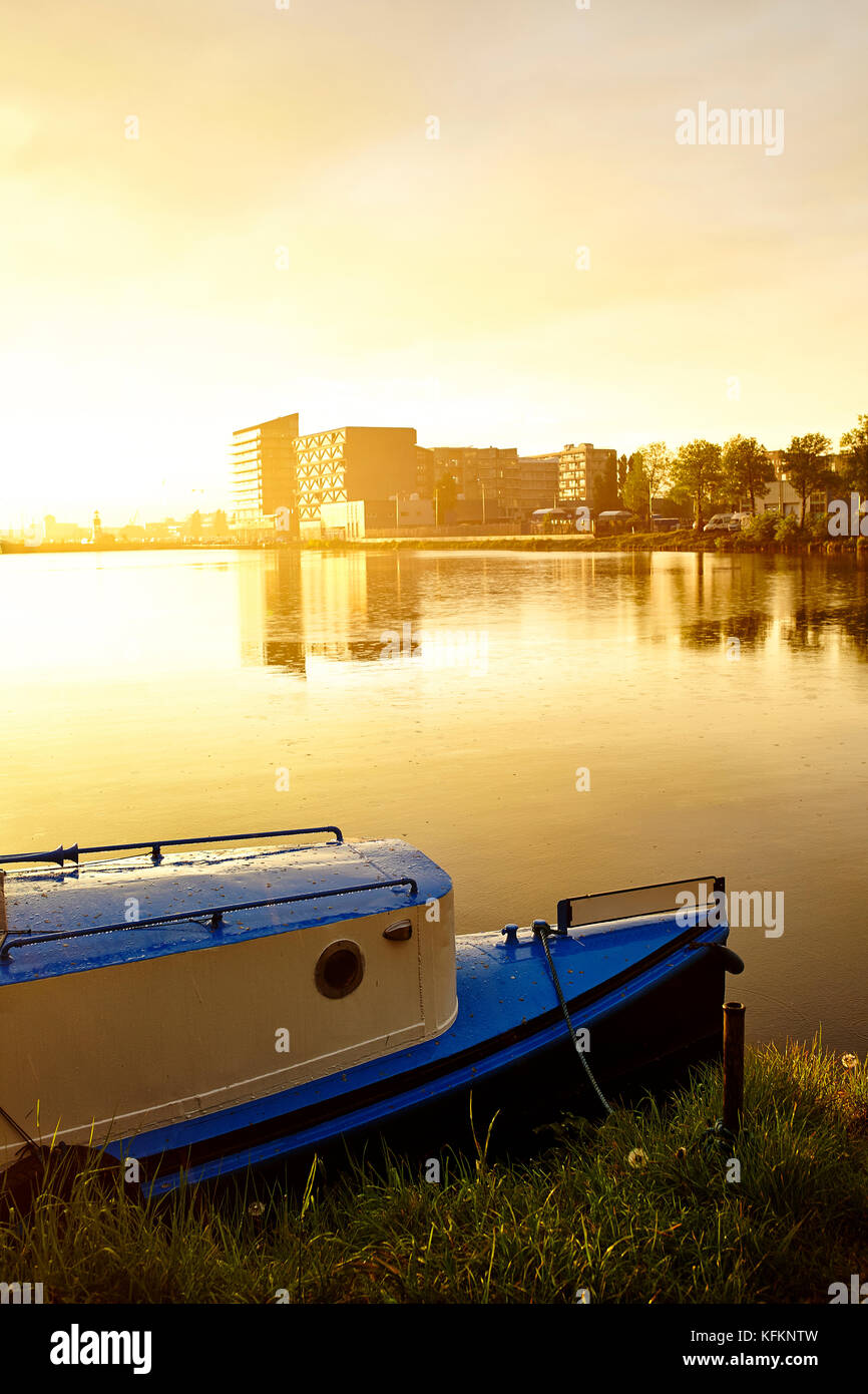 Kleine blaue niederländische Yacht in der Hintergrundbeleuchtung auf Kanal in Amsterdam Stockfoto