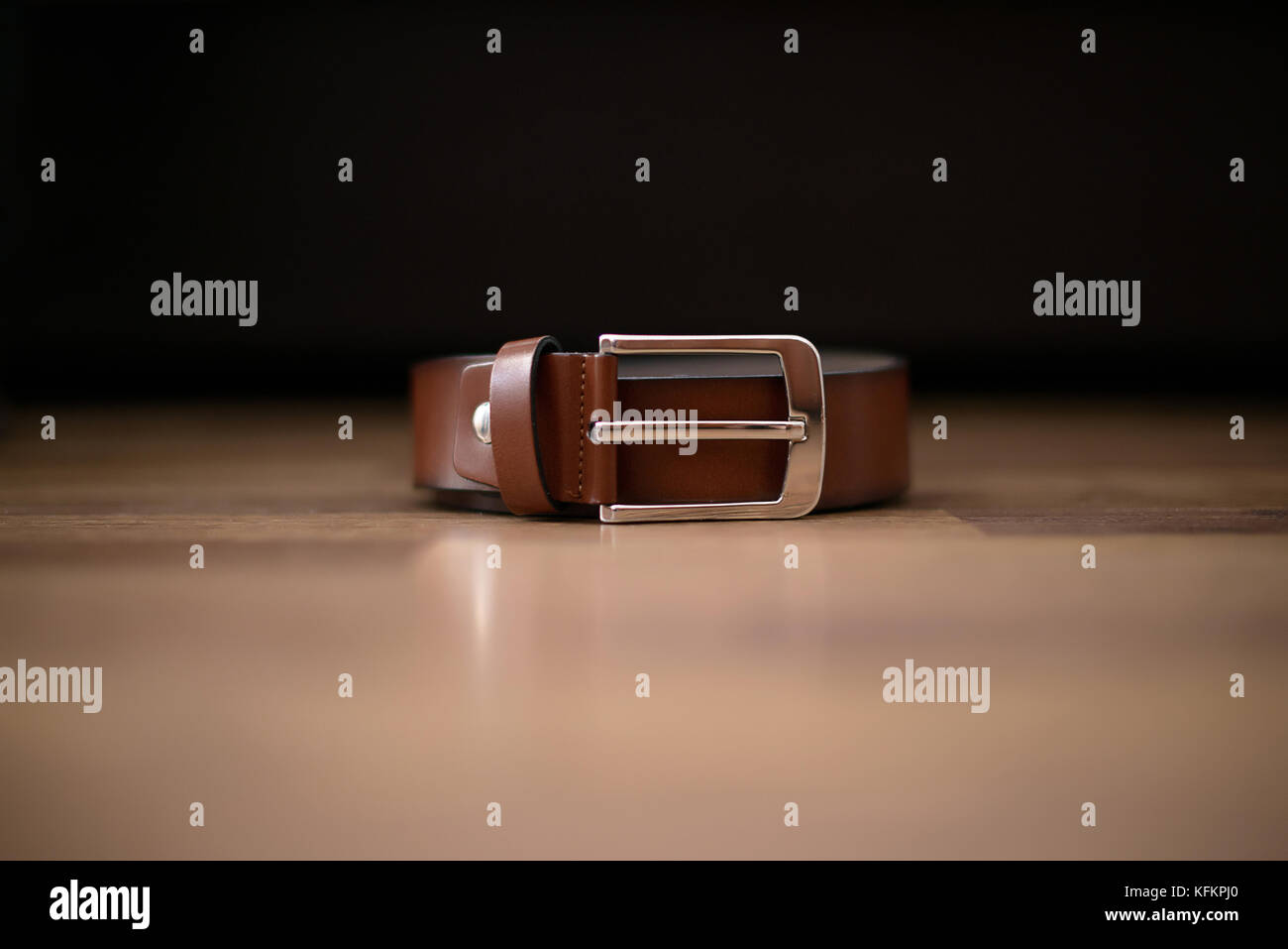 Isolierte business braun Leder Männliche Riemen mit sichtbaren silbernen Schnalle auf einem braunen Tisch mit dunklen Hintergrund einstellen Stockfoto