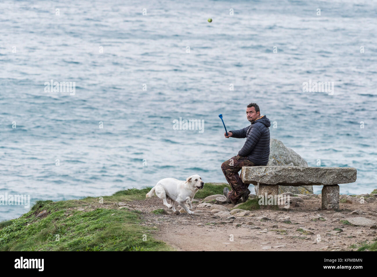 Hundespaziergängen - ein Mann wirft einen Ball für seinen Hund in Porth Nanven in Cornwall. Stockfoto