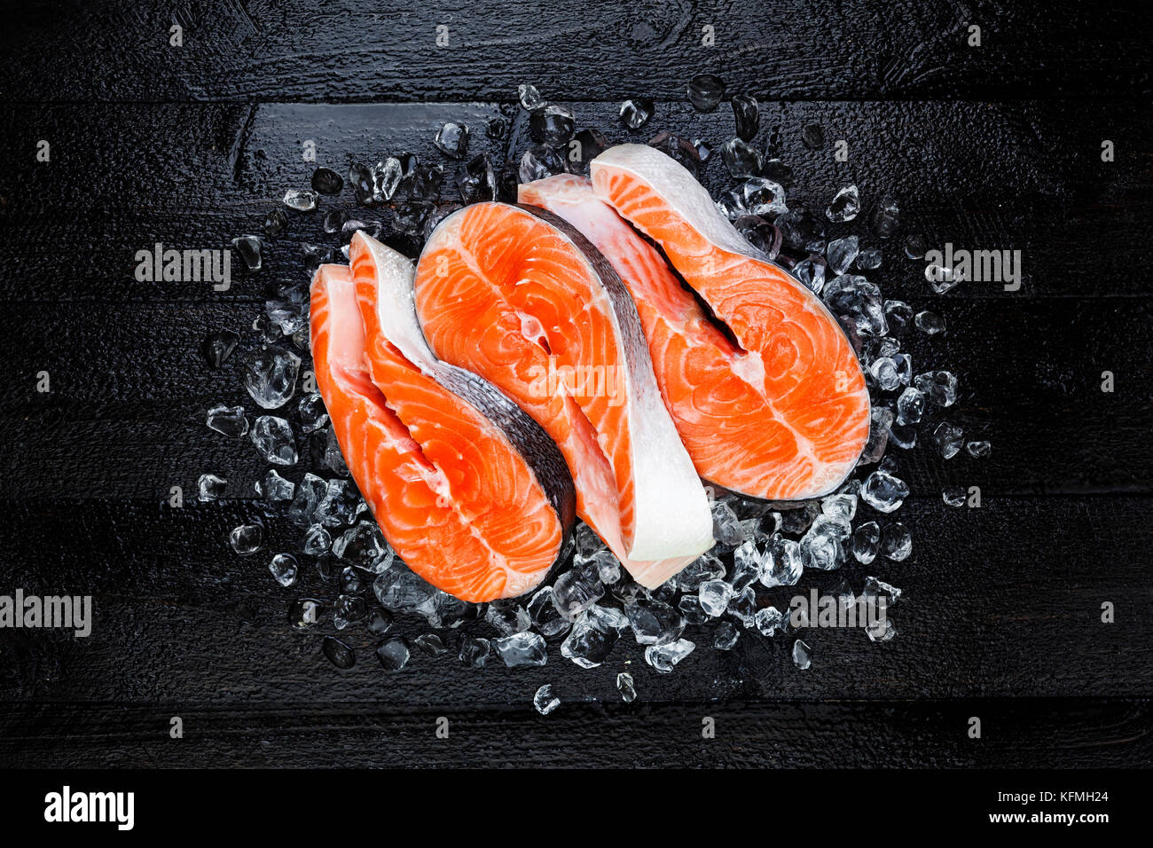 Frischen, rohen Lachs rot Fisch Steak auf Eis auf schwarzer Holztisch, Ansicht von oben Stockfoto