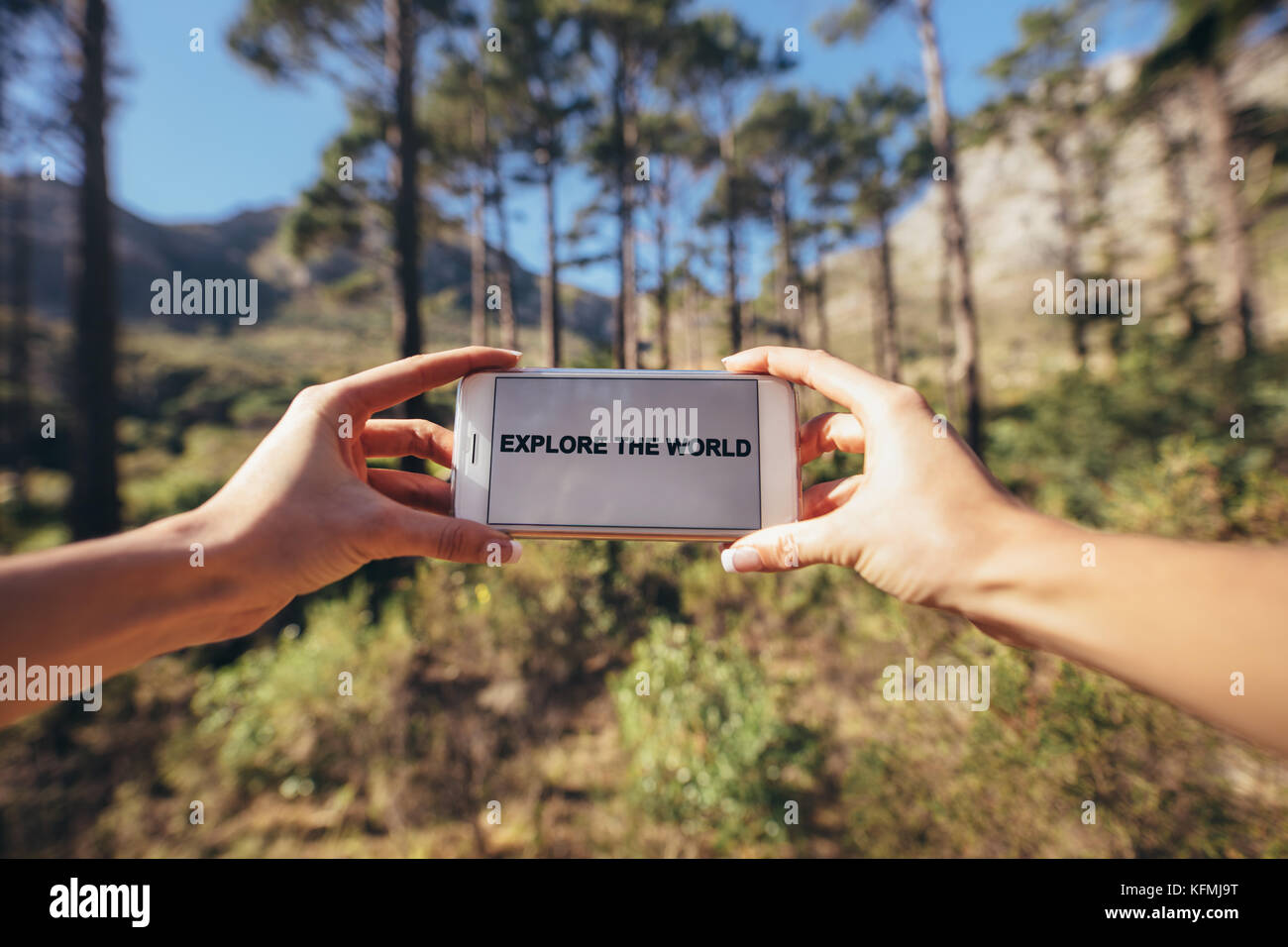 Hände halten ein smart phone gegen einen unscharfen Wald Hintergrund. Handy Bildschirm mit den Worten der Welt erkunden. Stockfoto