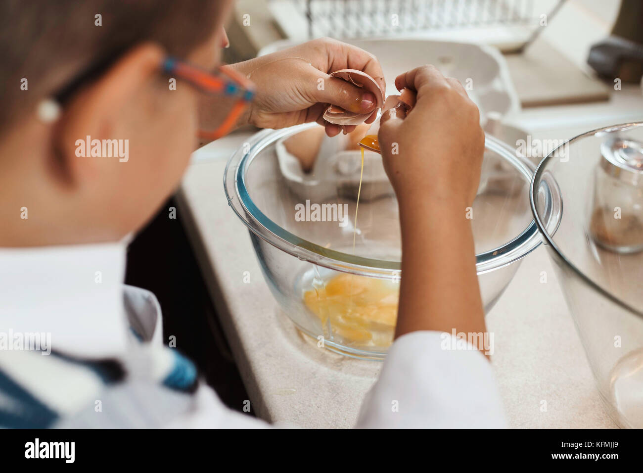 7-jähriger Junge Hilfe in der Küche, Aufschlagen der Eier in große Glasschüssel. Stockfoto