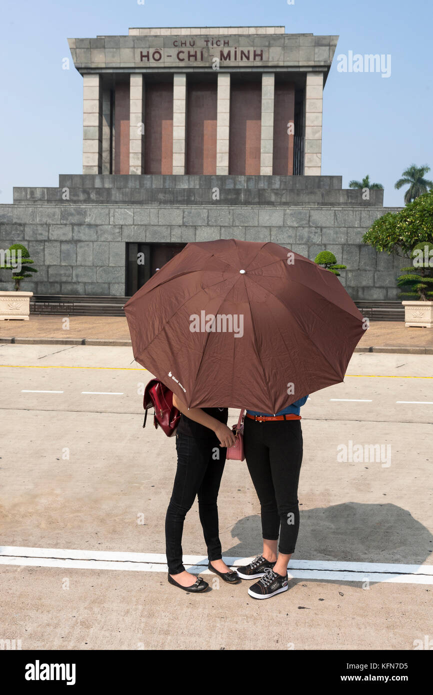 Zwei junge Studenten verstecken sich hinter einem Schirm vor dem beeindruckenden Ho Chi Minh Mausoleum, Hùng Vương, Điện Biên, Ba Đình, Hà Nội, Vietnam Stockfoto