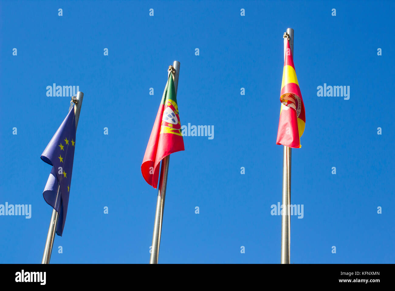 Zwei portugiesische Flaggen und eine europäische Flagge hängen in der ruhigen Luft eines ruhigen Tages vor einem Hotel in Albuferia in Portugal Stockfoto