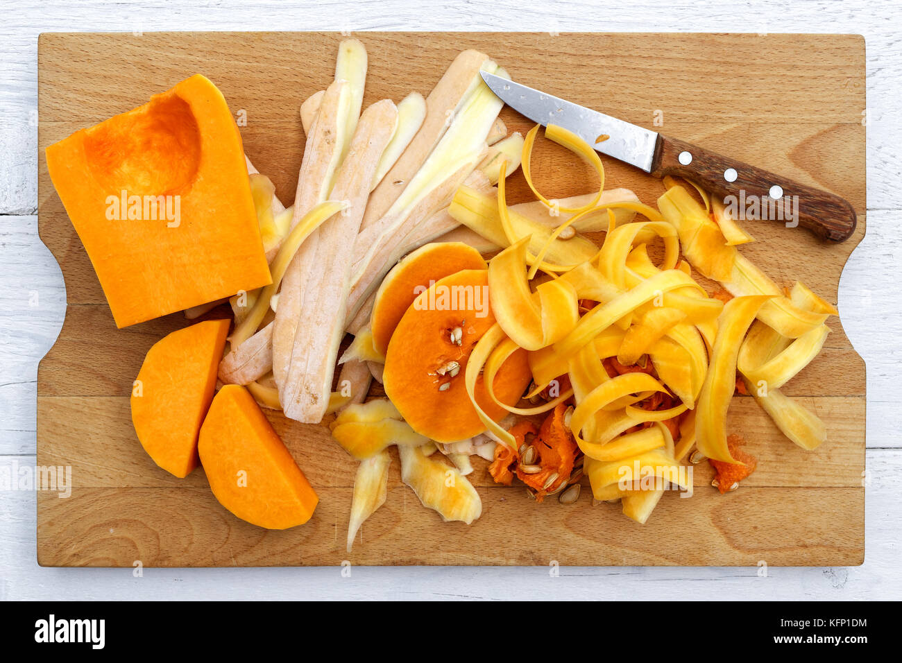 Schneiden, butternut Kürbis mit Schalen und Messer auf braunem Holz Schneidebrett auf weiß von oben isoliert. Stockfoto