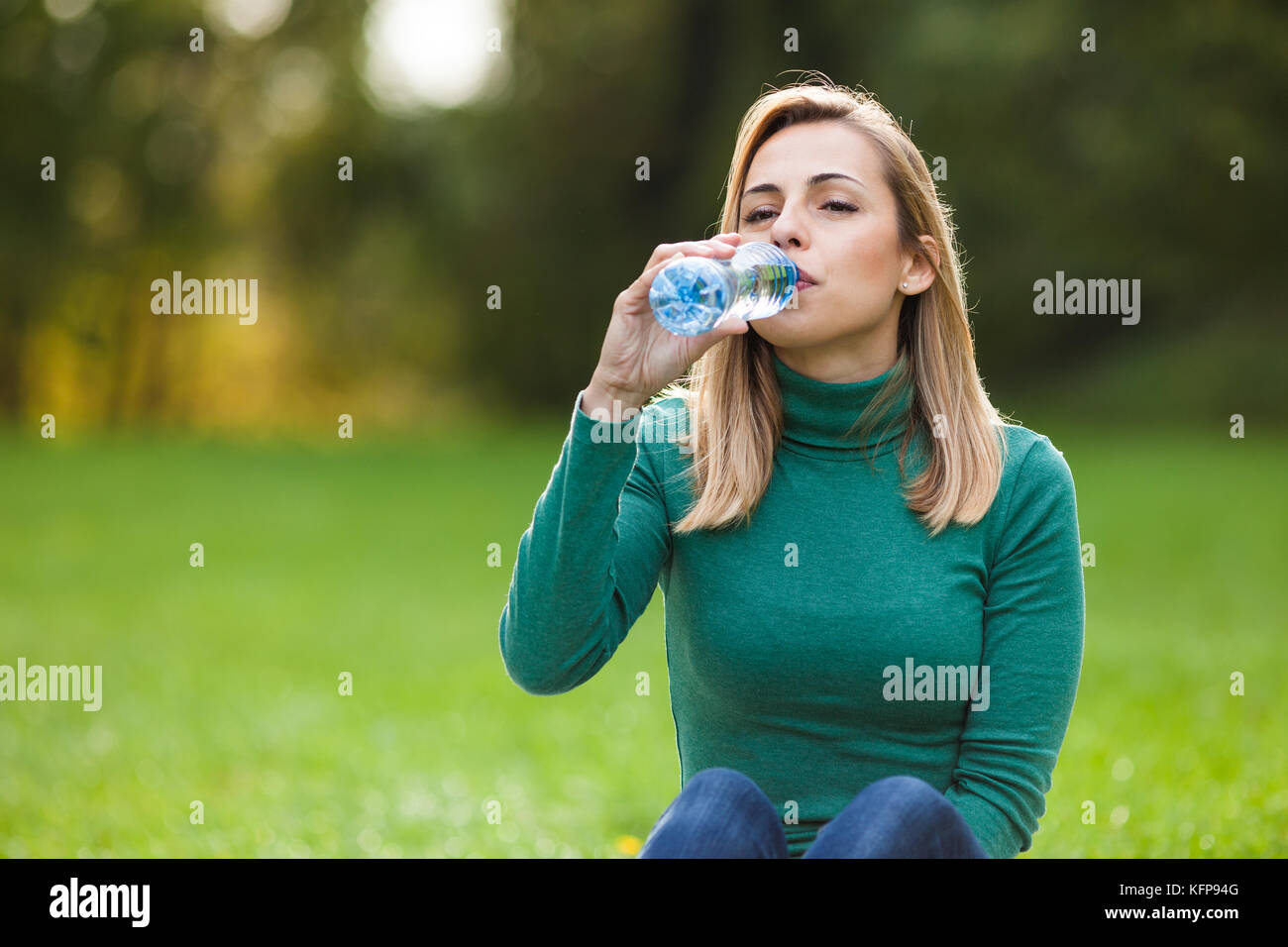Junge Frau trinkt Wasser im Park Stockfoto