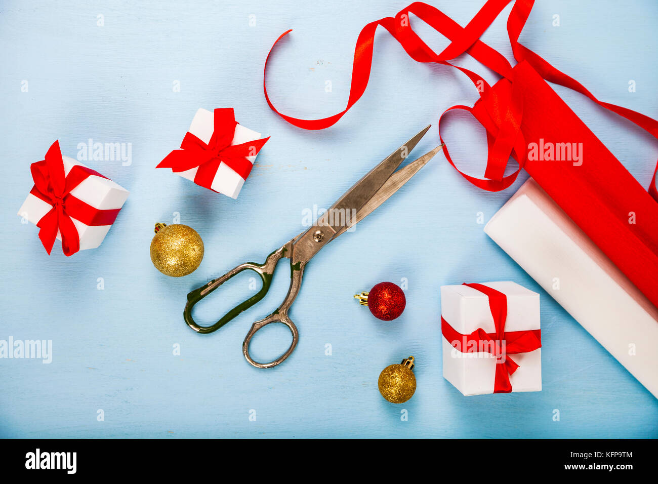 Die Verpackung der Weihnachtsgeschenke. Bänder, Papier, Schere und Ornamente auf einem blauen Holztisch. Stockfoto