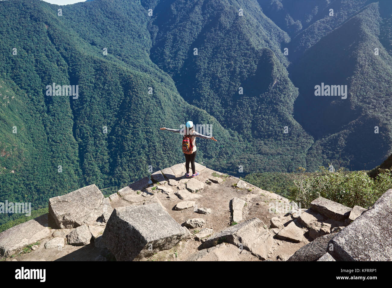 Glückliche junge Frau, Blick auf die Berge. Mädchen stehen auf Klippe mit Händen Stockfoto
